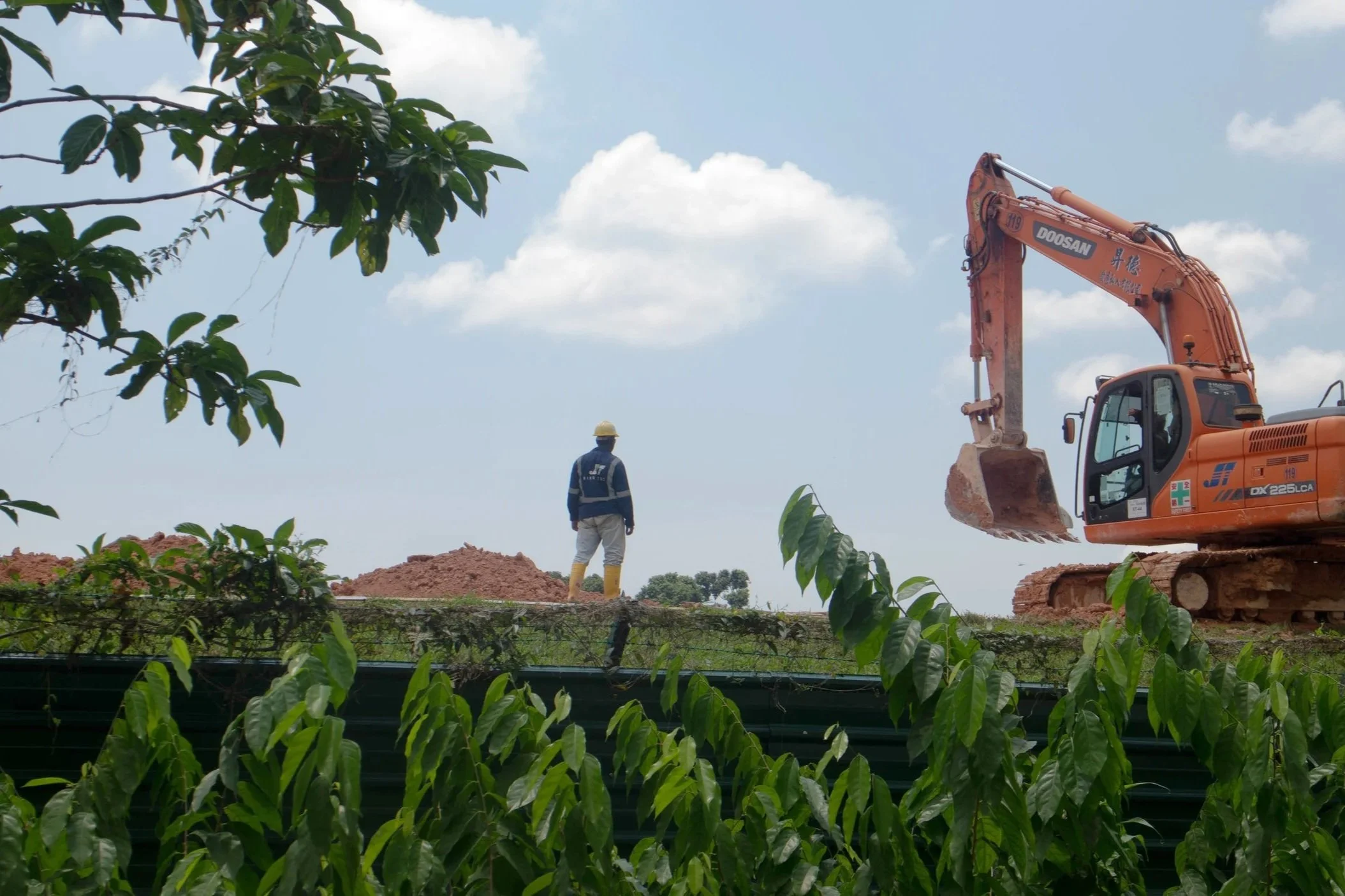 An orange excavator and a worker in a hard hat at a construction site for land clearing and earthmoving.