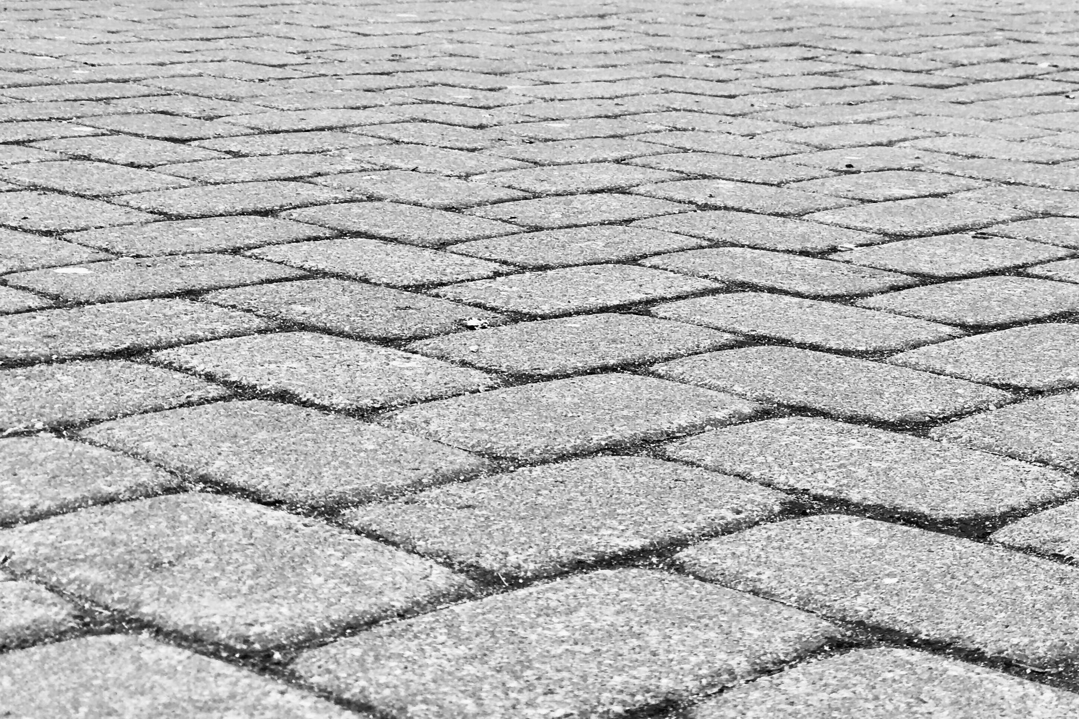 A close-up, ground-level view of textured gray cobblestone pavers laid in a classic pattern for a driveway or patio.