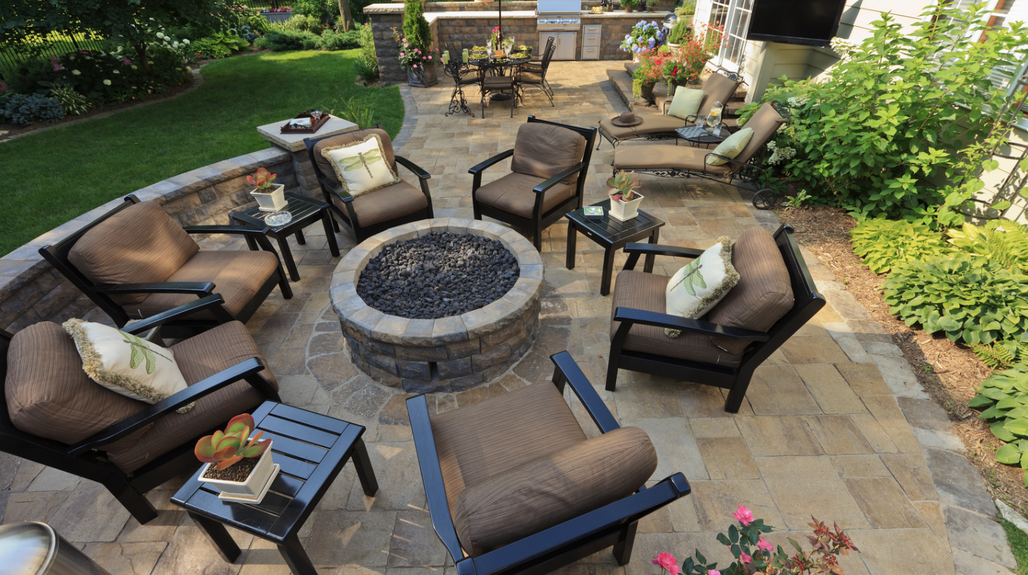 A circular stone fire pit is surrounded by brown cushioned armchairs and small black side tables on a paved patio with a "Hardscaping" text overlay.