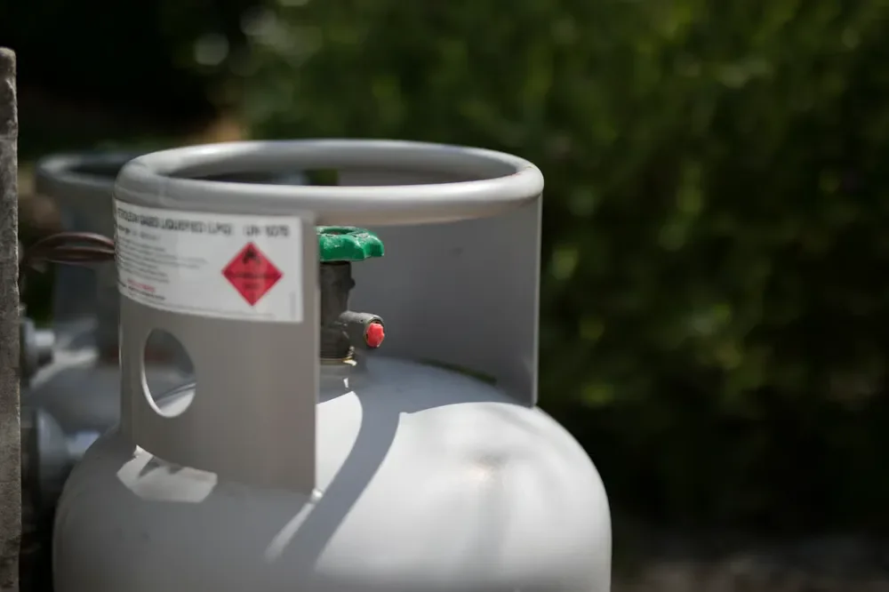Close-up of a grey liquefied petroleum gas LPG cylinder with a green valve handle and safety warning label.
