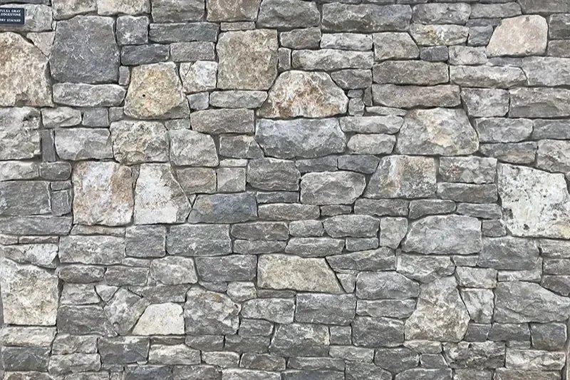 Texture of a professionally installed stacked stone wall featuring various sizes of natural gray and tan fieldstone.
