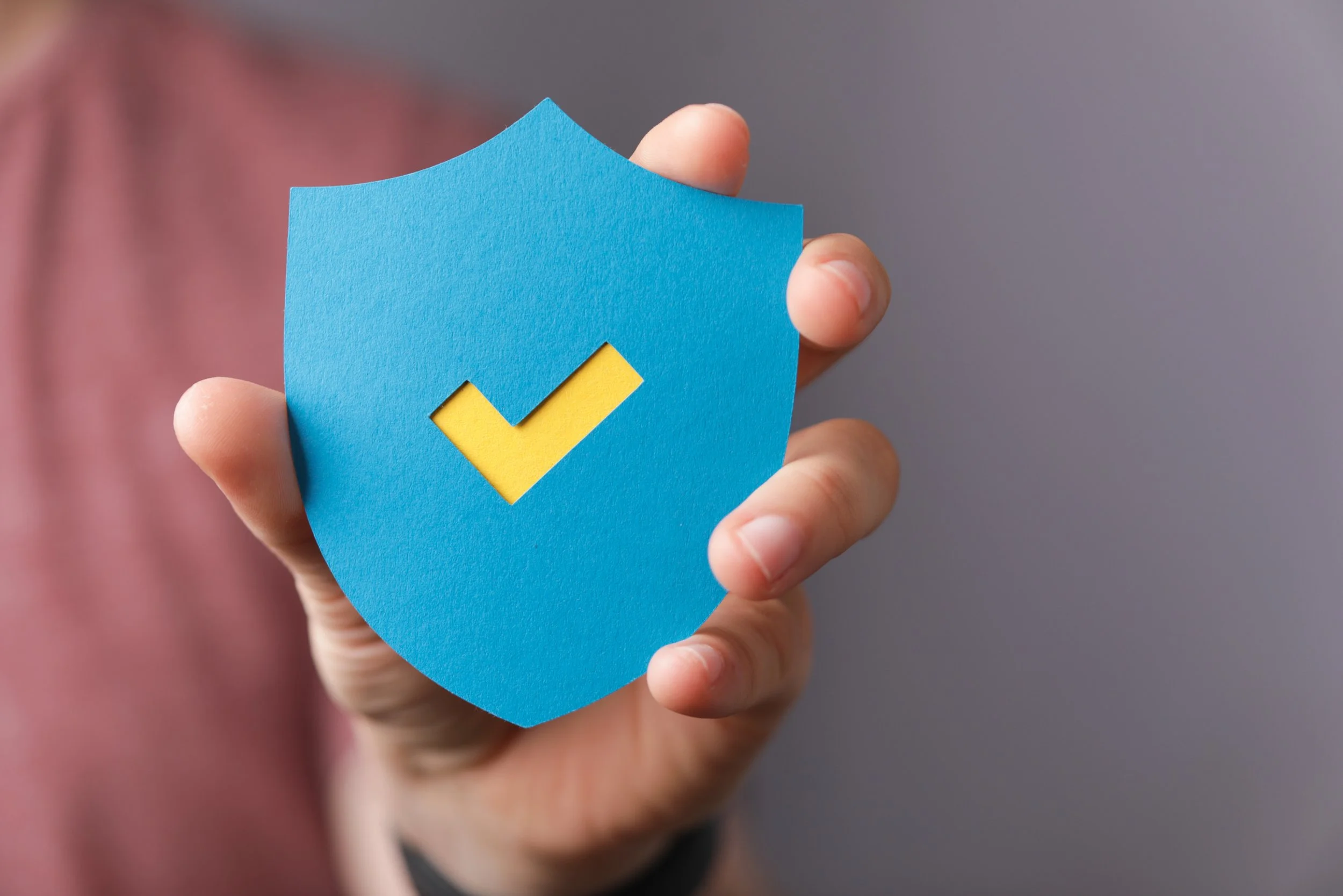 Hand holding a blue shield icon with a yellow checkmark, representing professional service guarantees and security.
