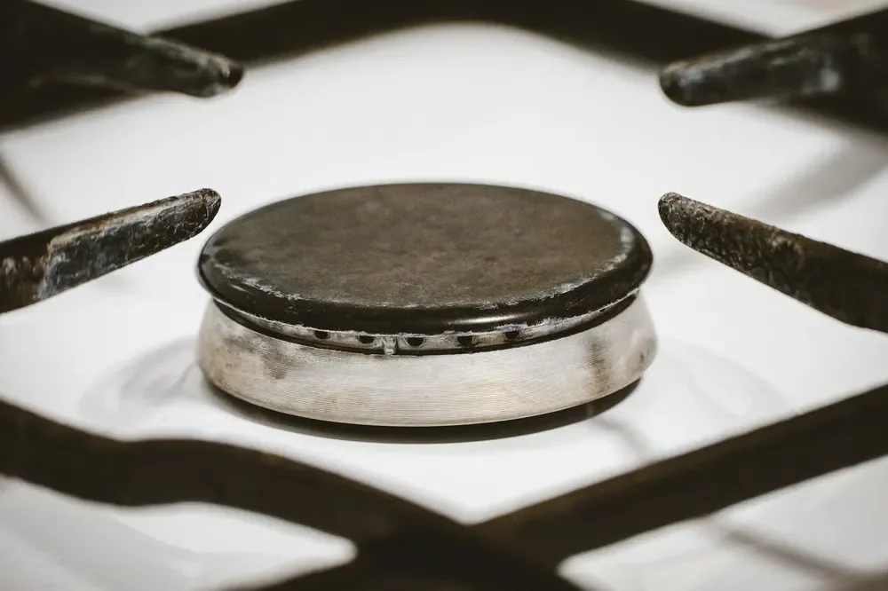 Close-up view of a clean, unlit gas stove burner with dark metal grates on a white kitchen cooktop.