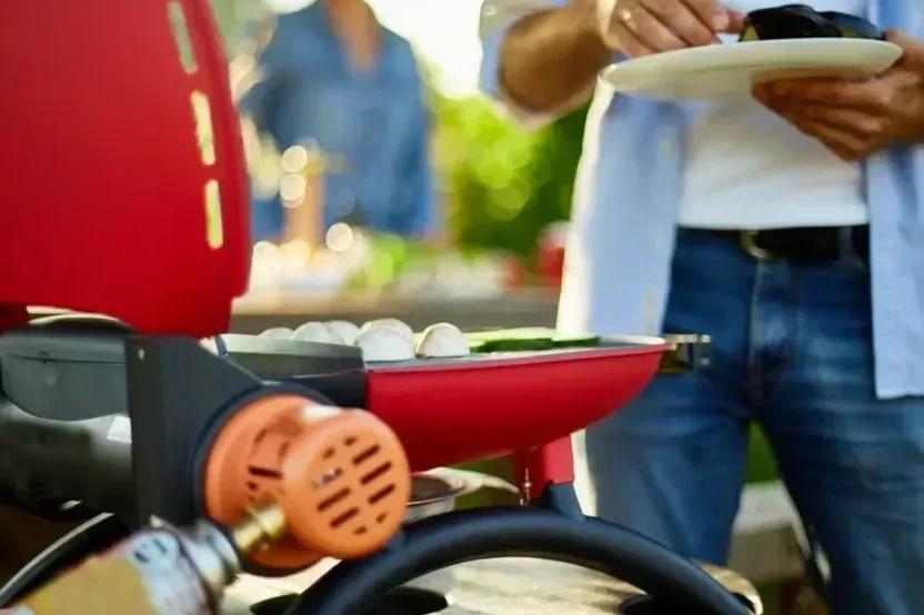Portable red propane gas grill being used for outdoor cooking.