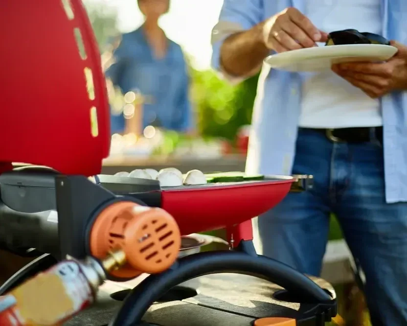 Close-up of food cooking on a red portable gas grill during a backyard patio barbecue.
