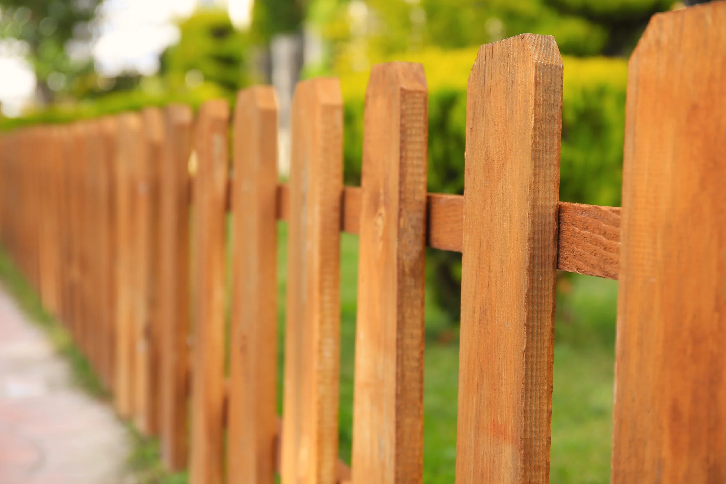 Close-up of a stained cedar wood picket fence bordering a green lawn and garden.