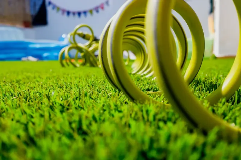 Coiled yellow garden hose resting on bright green grass for lawn watering and irrigation.