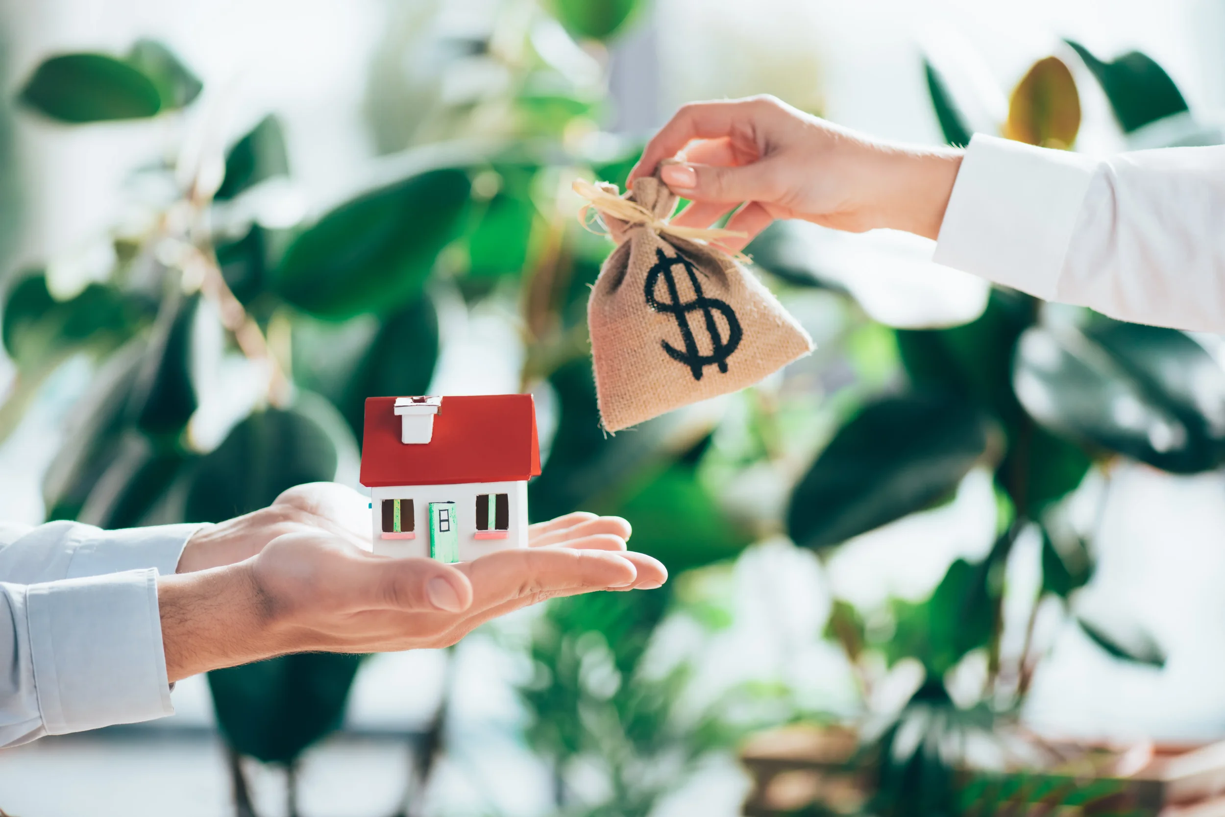 Hands exchanging a small house model and a bag of money, representing a property sale or real estate investment.
