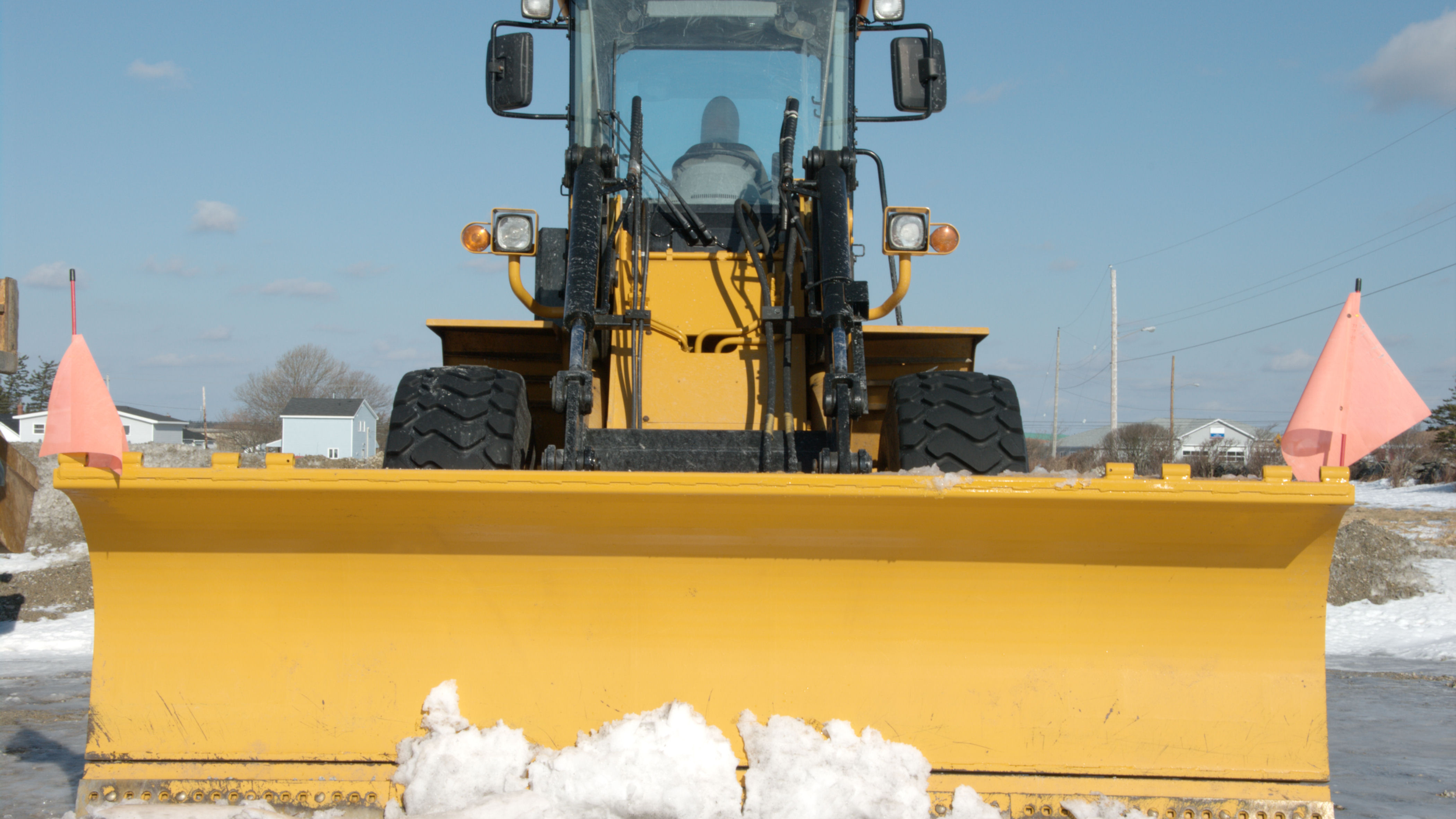 Front view of a heavy-duty yellow wheel loader with a large snow plow attachment clearing an industrial lot.