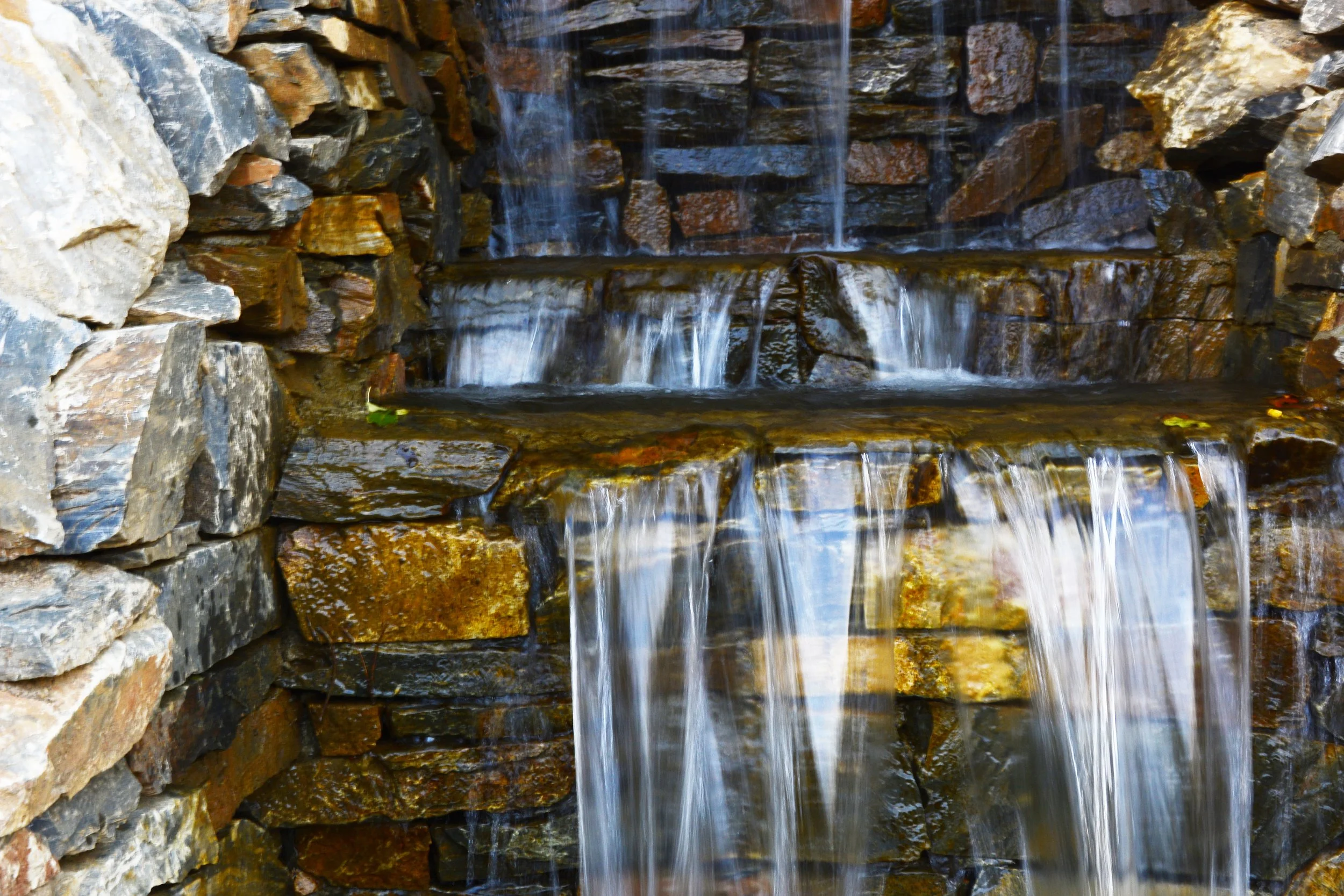 A multi-tiered outdoor waterfall cascading over stacked natural stones and rocks.