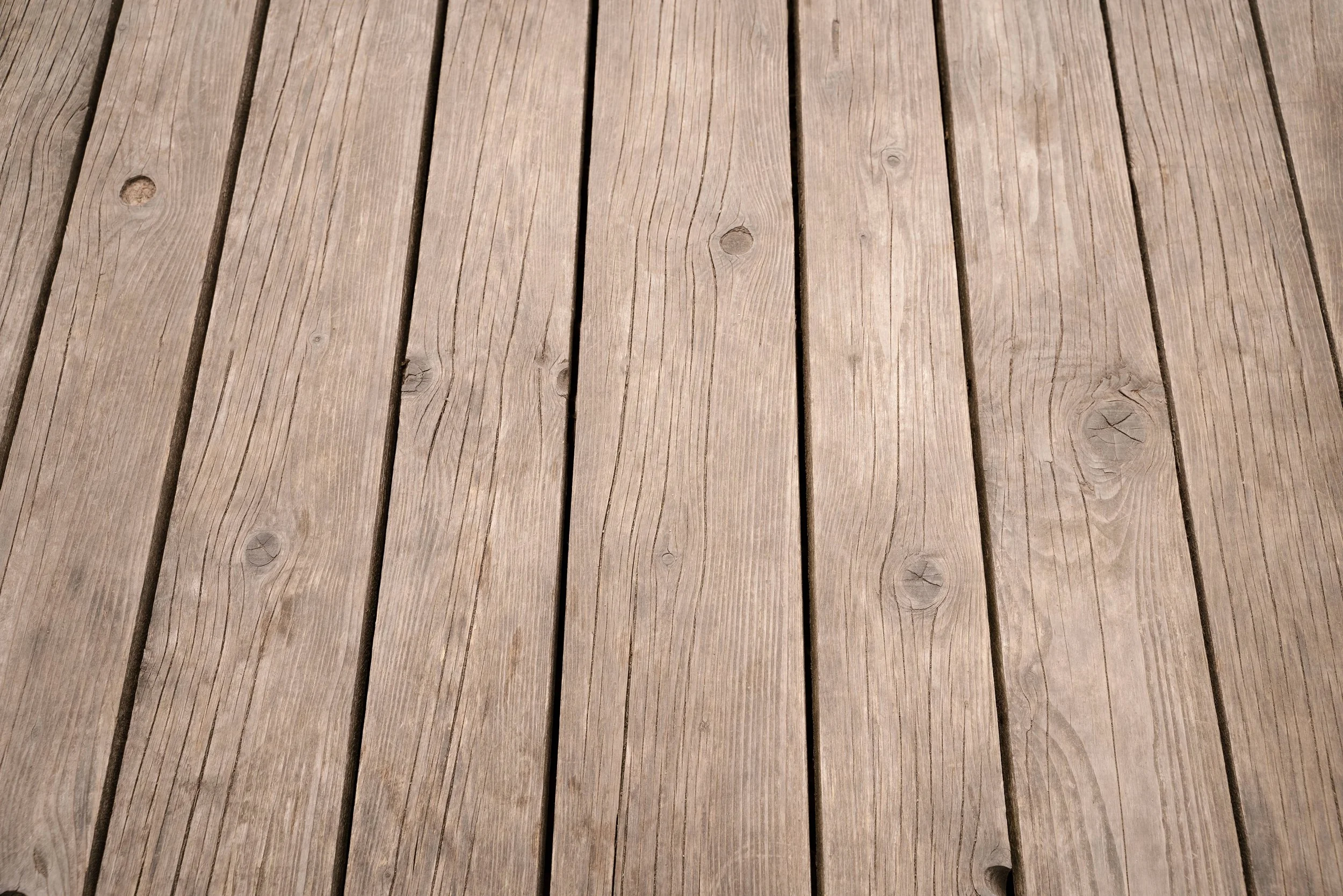 Close-up texture of weathered natural wood deck boards with visible grain and knots.