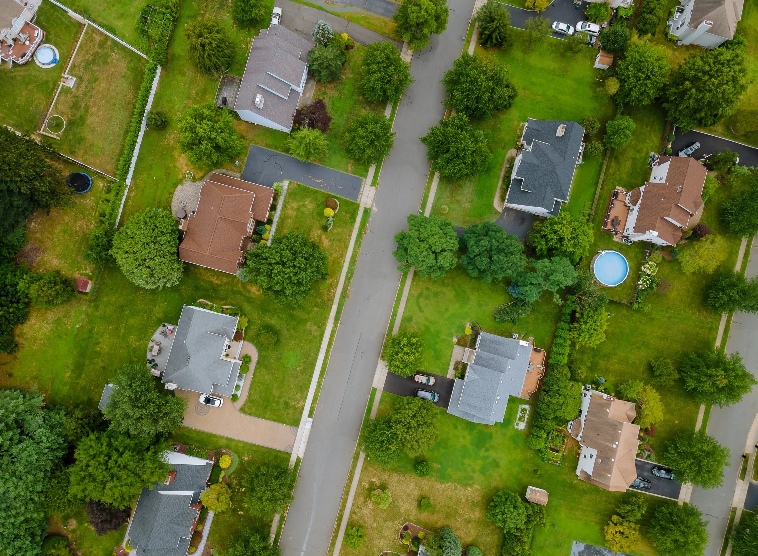 Aerial view of a suburban neighborhood showing houses with lush green lawns and a central roadway.