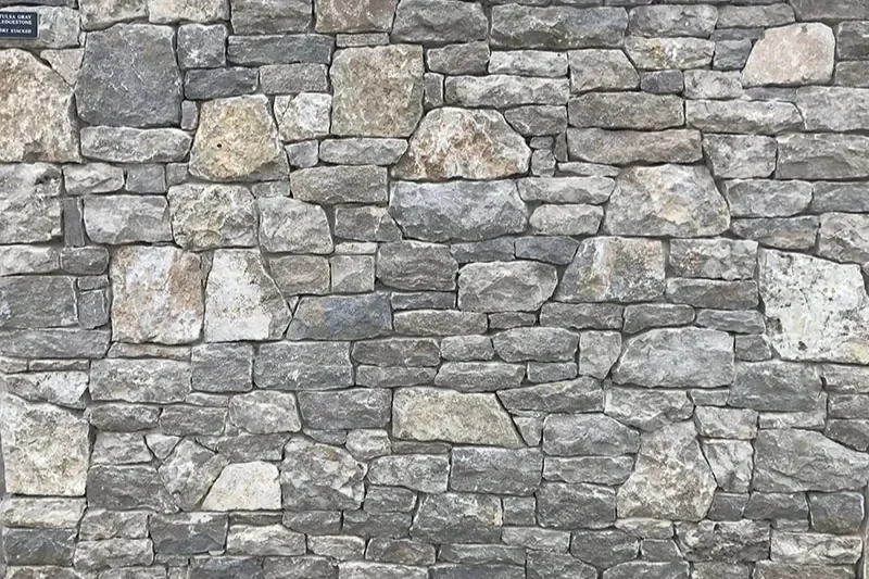 Detailed view of a custom-built natural fieldstone wall with varying gray and tan stones.
