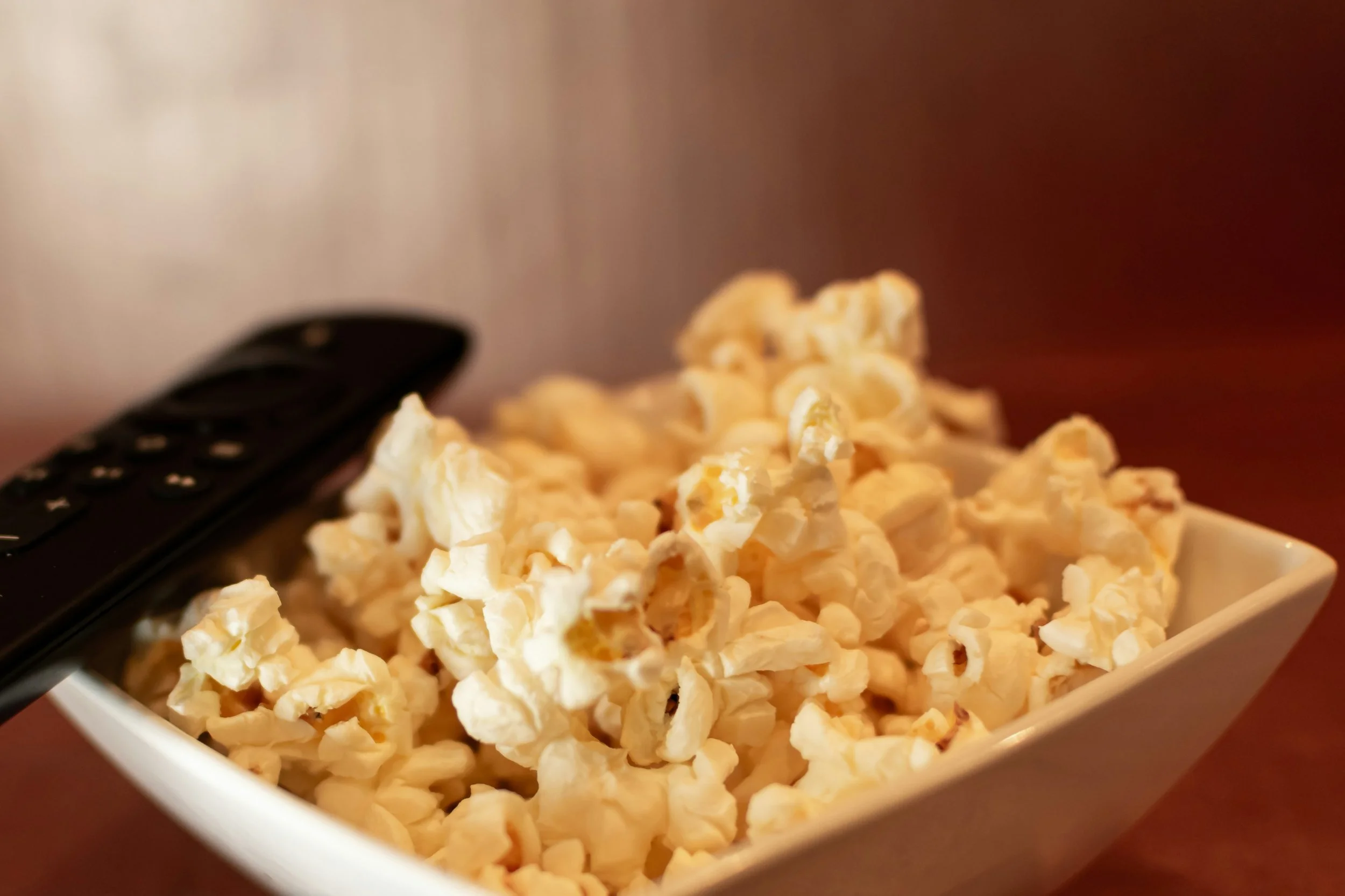 A bowl of homemade popcorn and a remote resting on a worn couch armrest