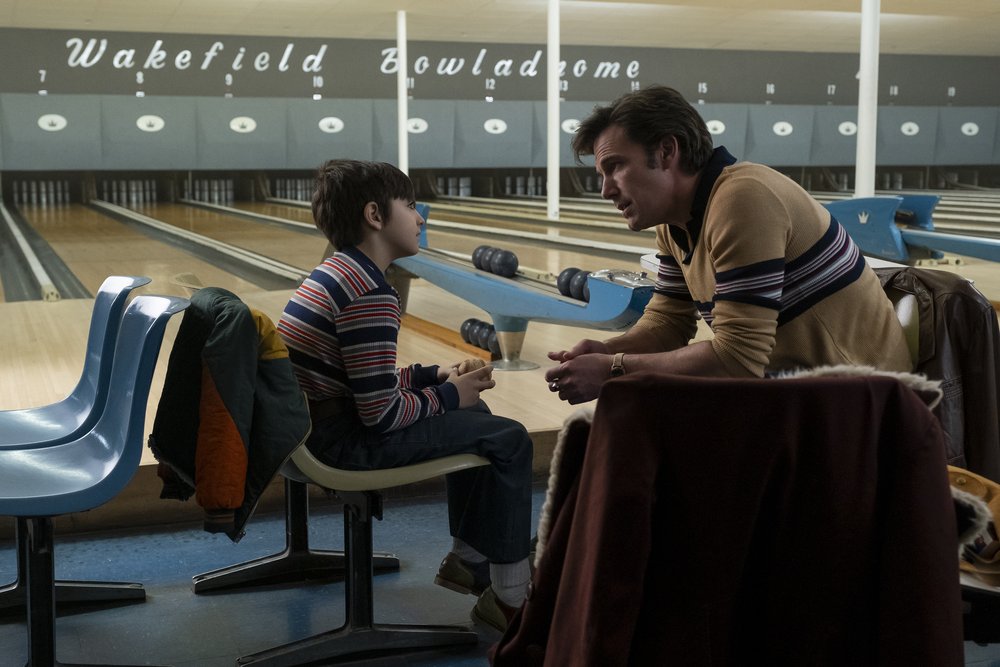 A man talks to a young boy in a bowling alley.