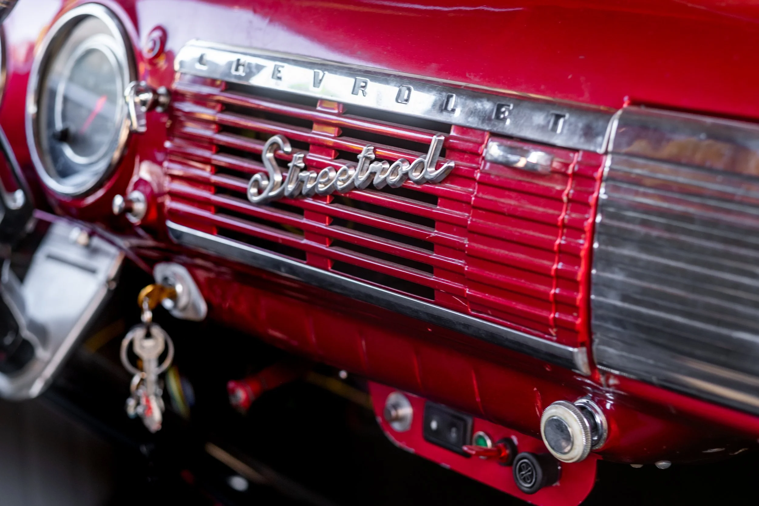 Close-up of the front grille of a red vintage Chevrolet streetrod car, displaying the Chevrolet badge and intricate chrome details.