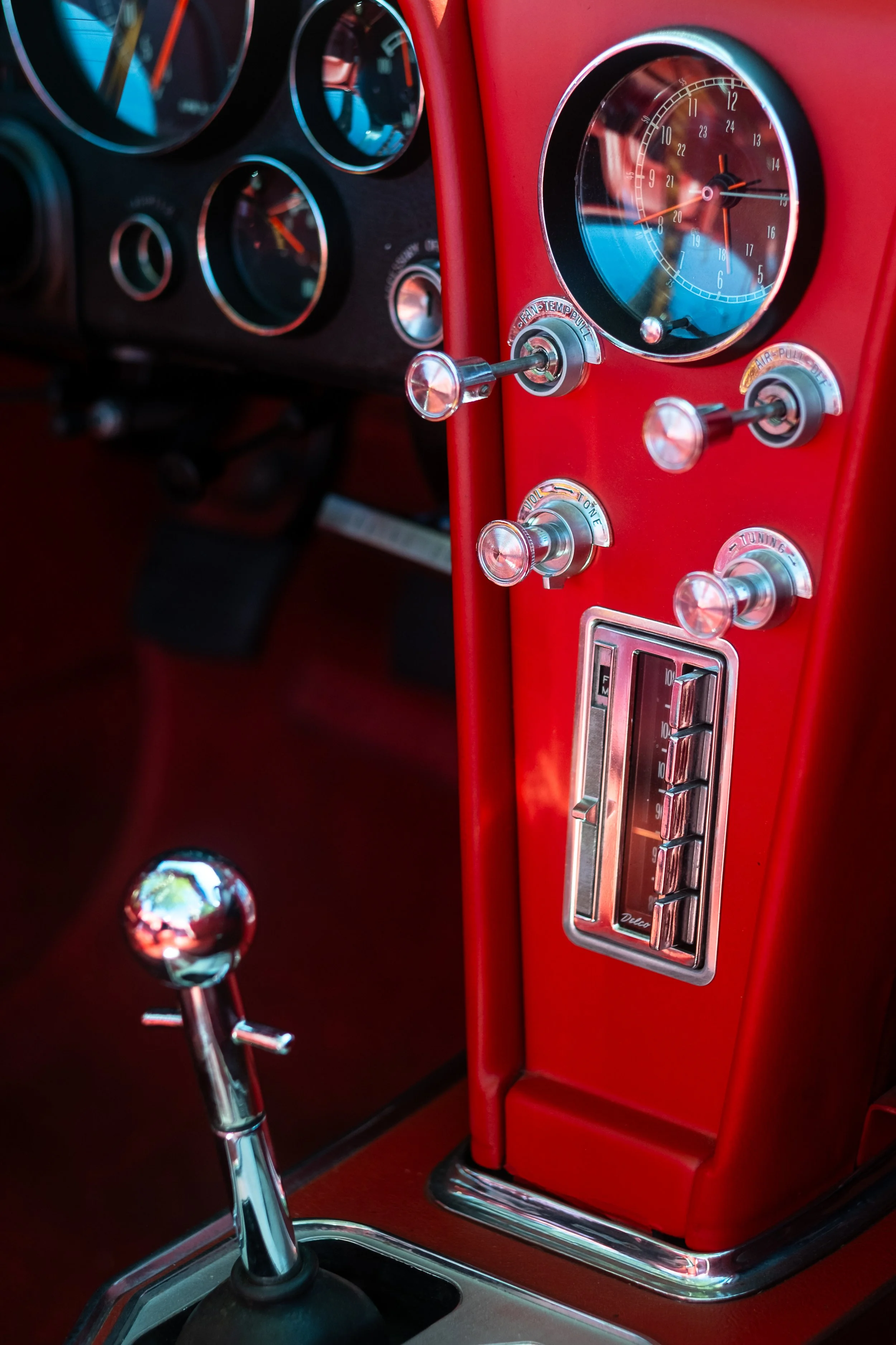 Close-up of the dashboard and gear shift of a vintage red car, featuring analog gauges, chrome controls, and a red interior.