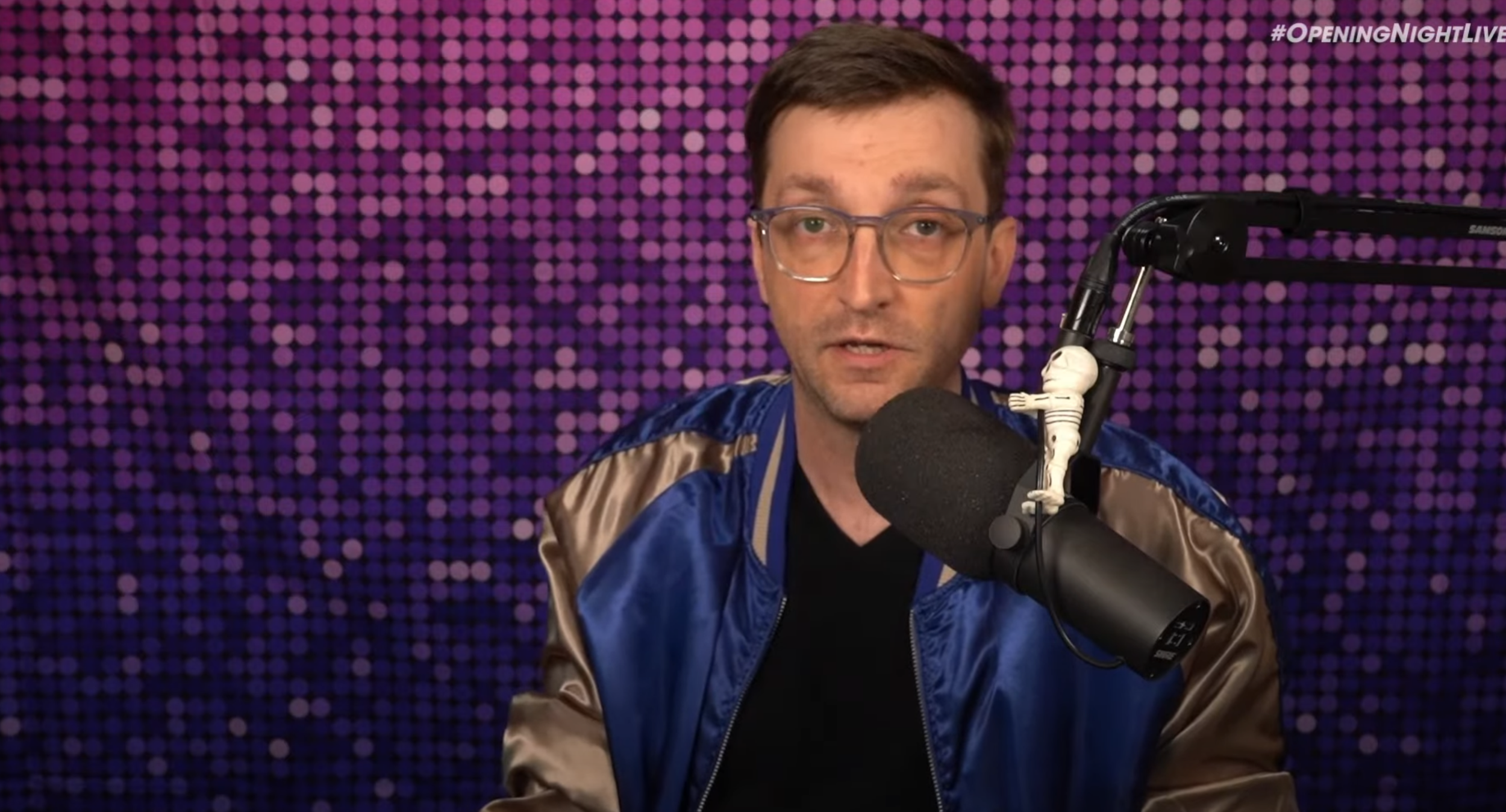 Kyle Bosman wearing a blue and gold jacket talking to the camera during the Opening Night Live Pre-show broadcast