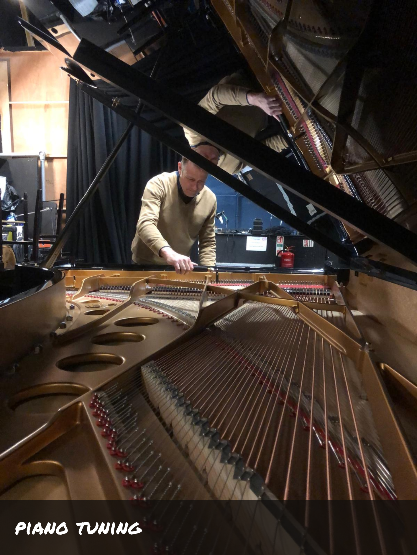 Someone stood by a grand piano tuning it