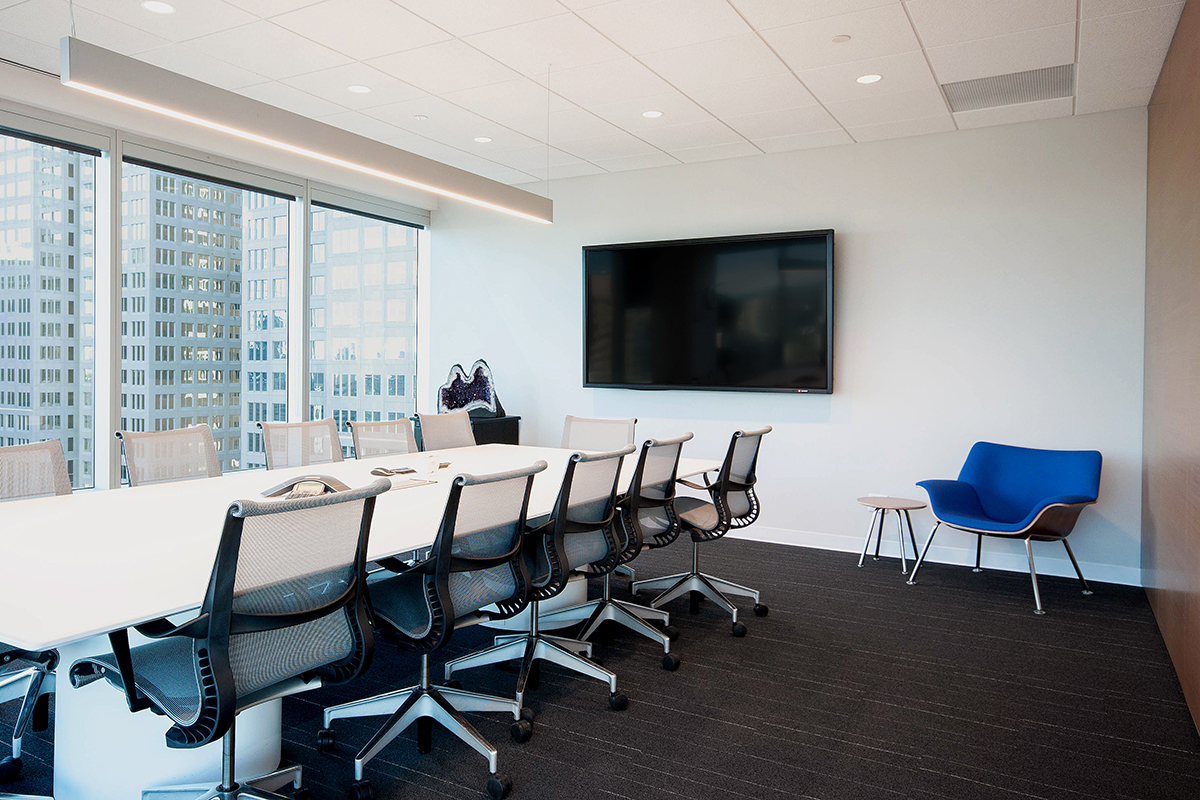 Clean lines and crisp finishes define the final design for this corporate office renovation project. An exposed-edge plywood reception desk anchors the space with custom rugs, Herman Miller furniture, and Modularts dividers complimenting it.