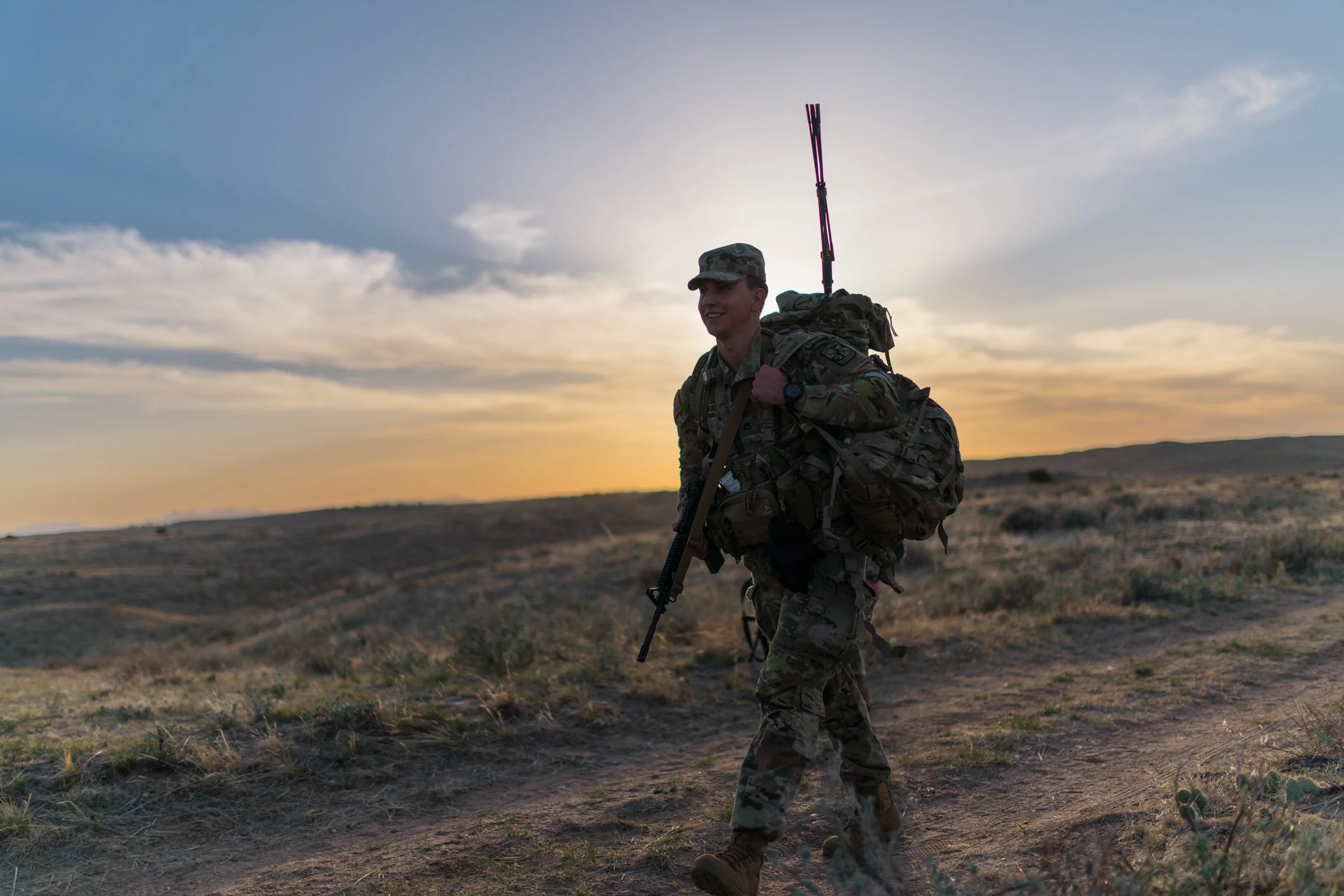 Soldier with rifle and pack silhouetted against dramatic desert sunset, editorial military photography
