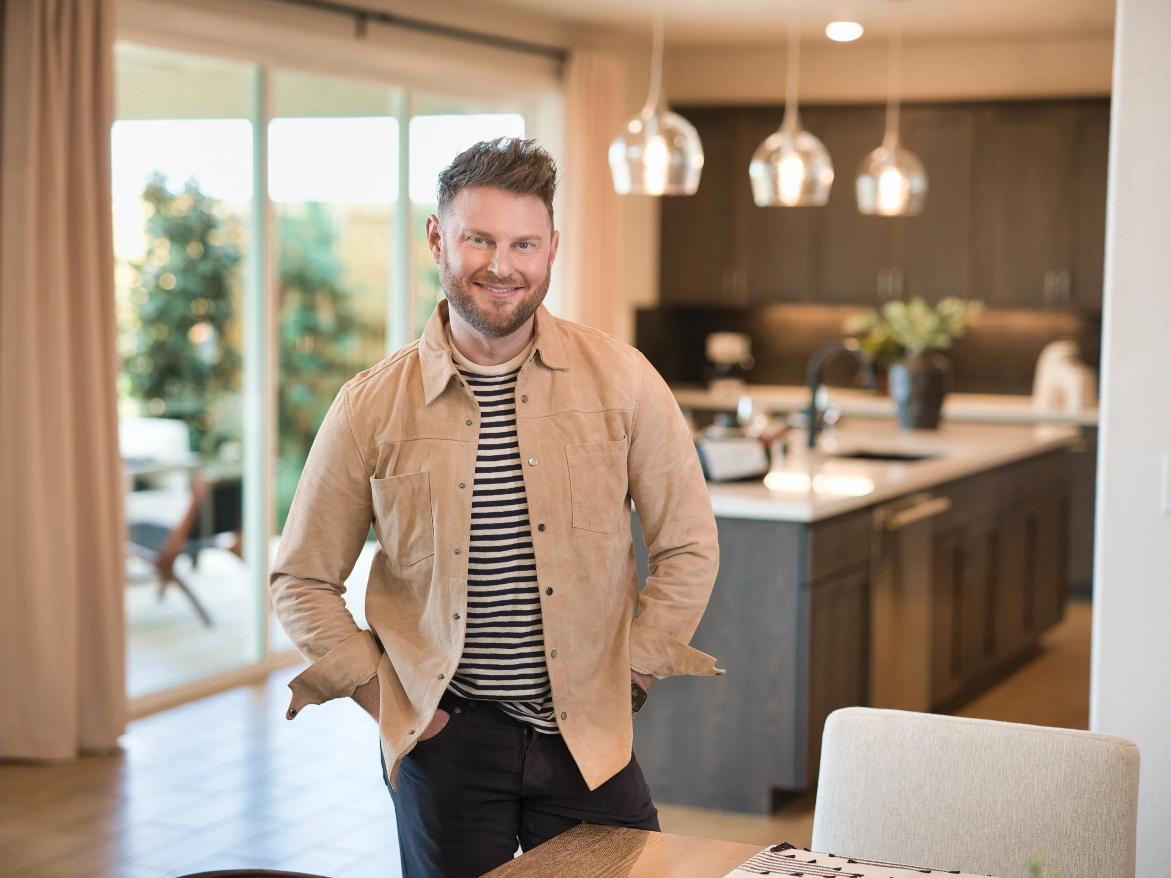 A portrait of a man standing in the kitchen with a casual outfit