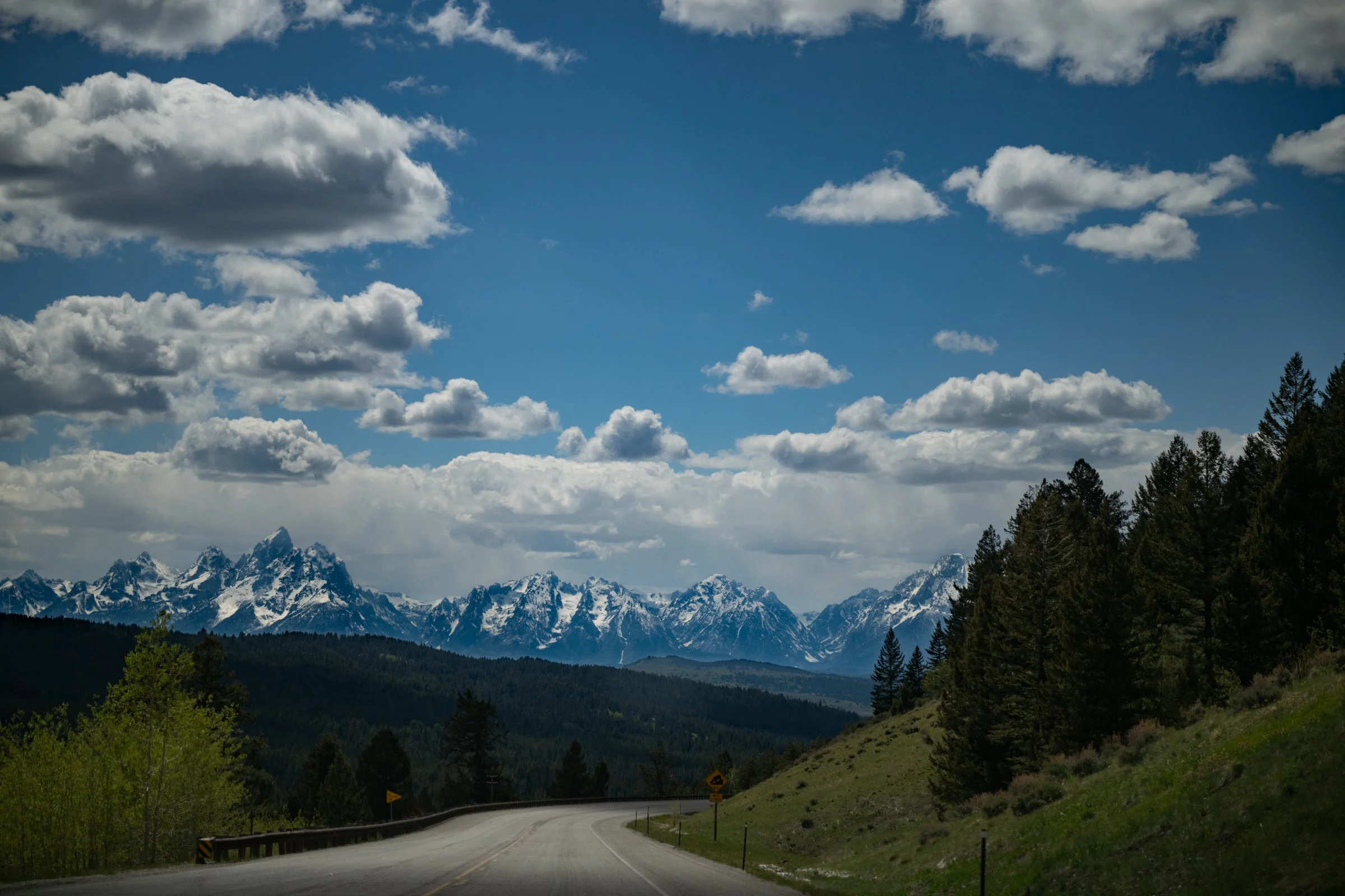 Highway curving toward the snow-capped Grand Teton mountain range under dramatic storm clouds in Wyoming