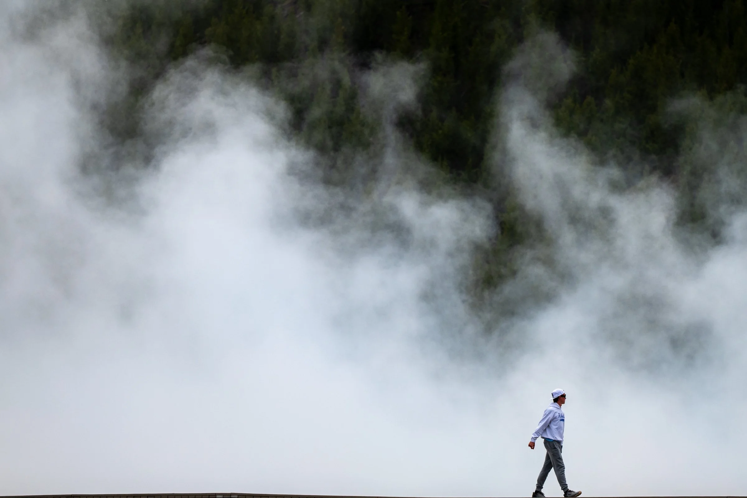 Single visitor walking along a boardwalk surrounded by dense geothermal steam at Yellowstone National Park
