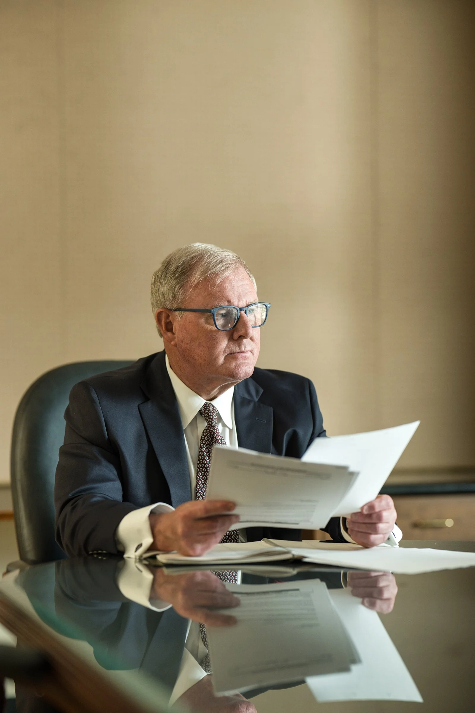 Senior male executive in suit reviewing documents at a traditional wood desk