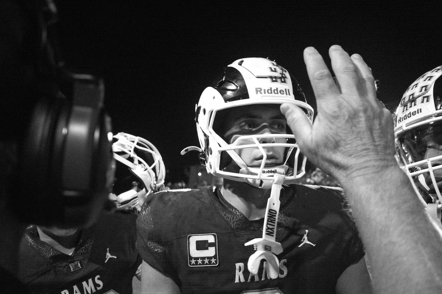 Black-and-white close-up of a coach's hand on a football player's helmet on the sideline, shot with a Viltrox 28mm