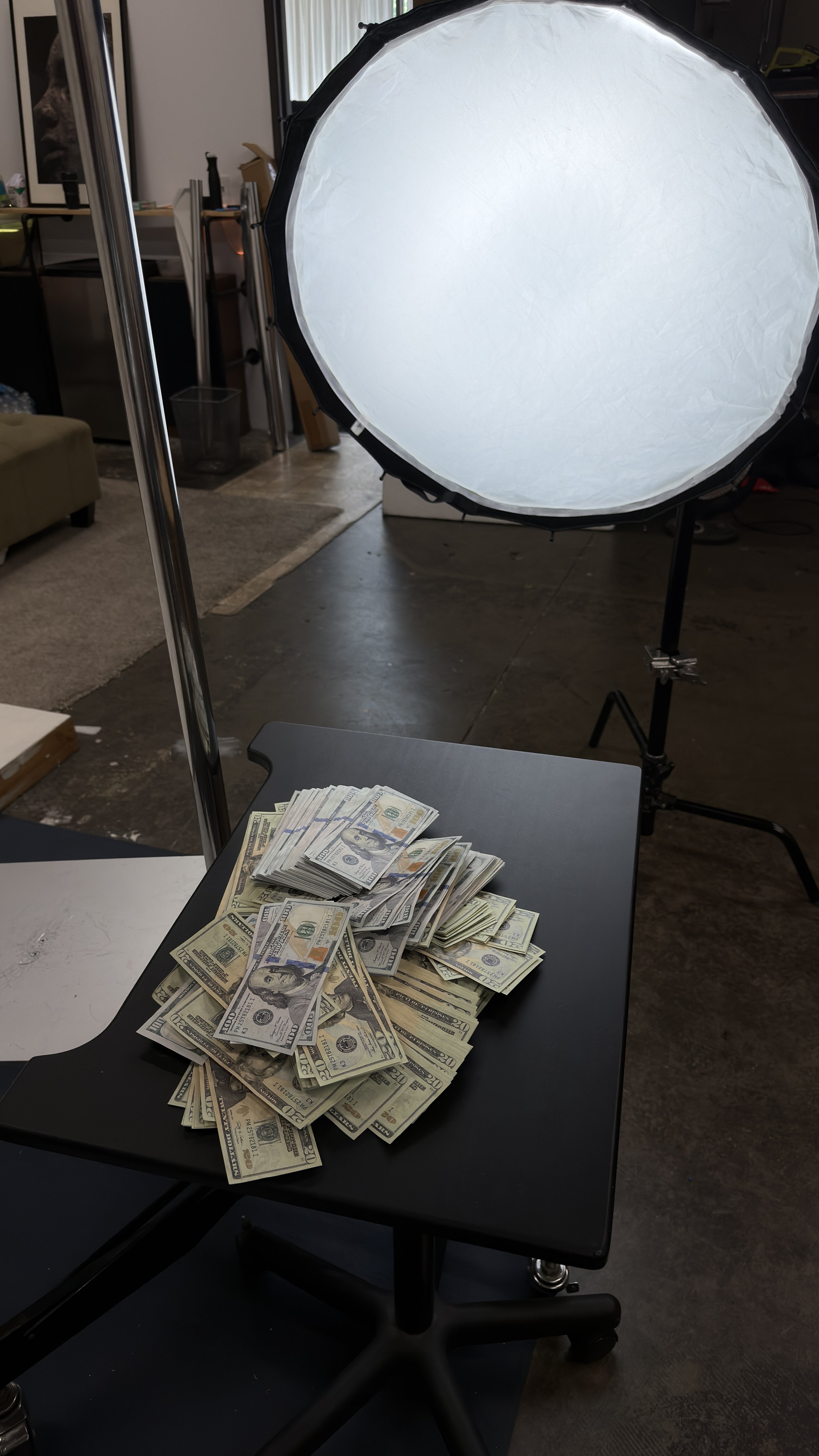 Professional studio setup with softbox lighting rig positioned over black table with prop money for high-value item documentation
