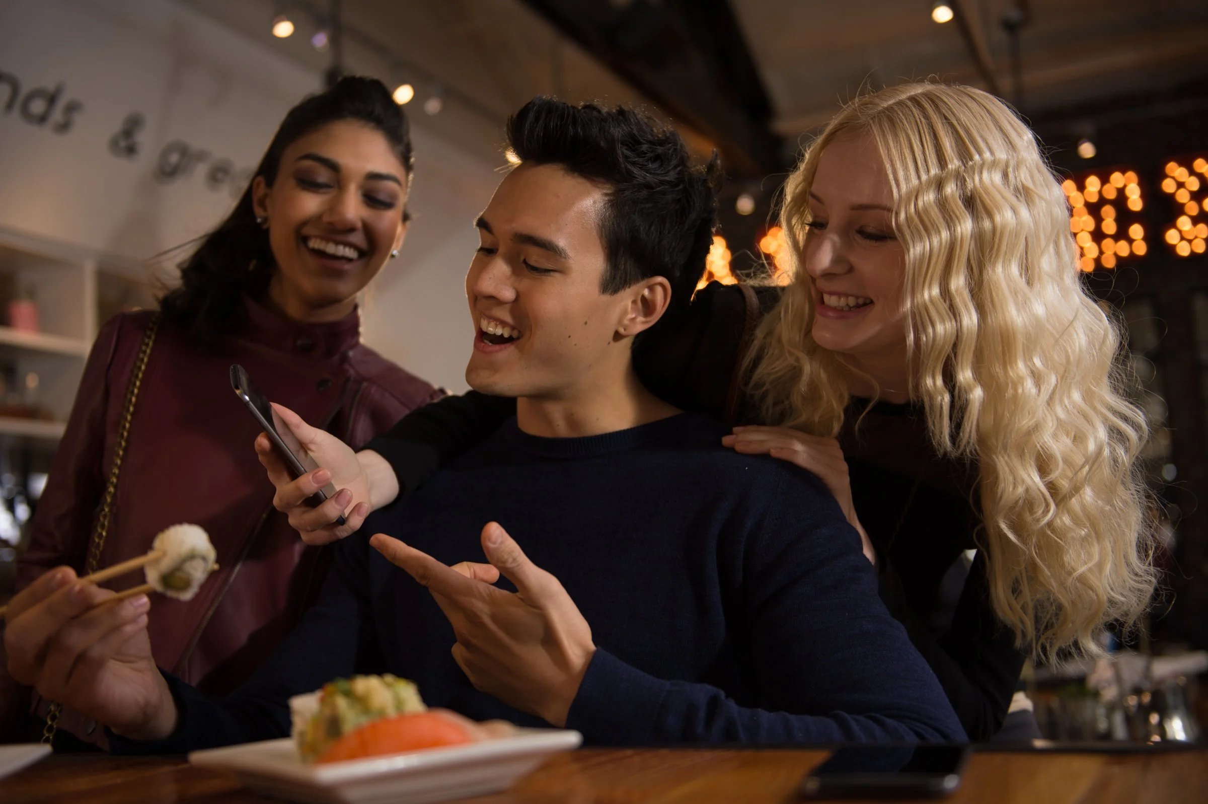 Three friends laughing and sharing food at restaurant, lifestyle commercial photography