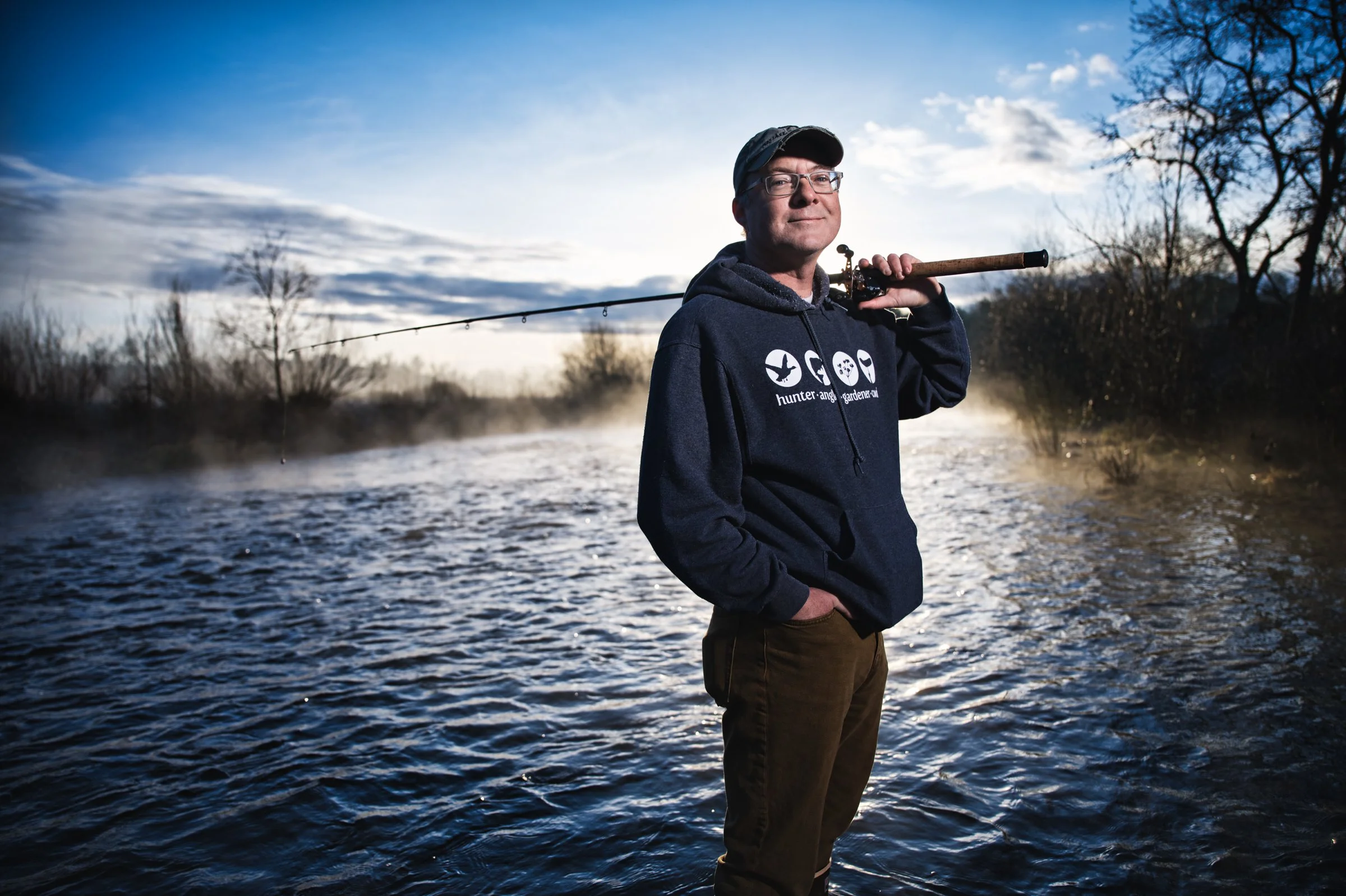 Man standing beside river at dusk with fishing rod, editorial outdoor portrait Sacramento