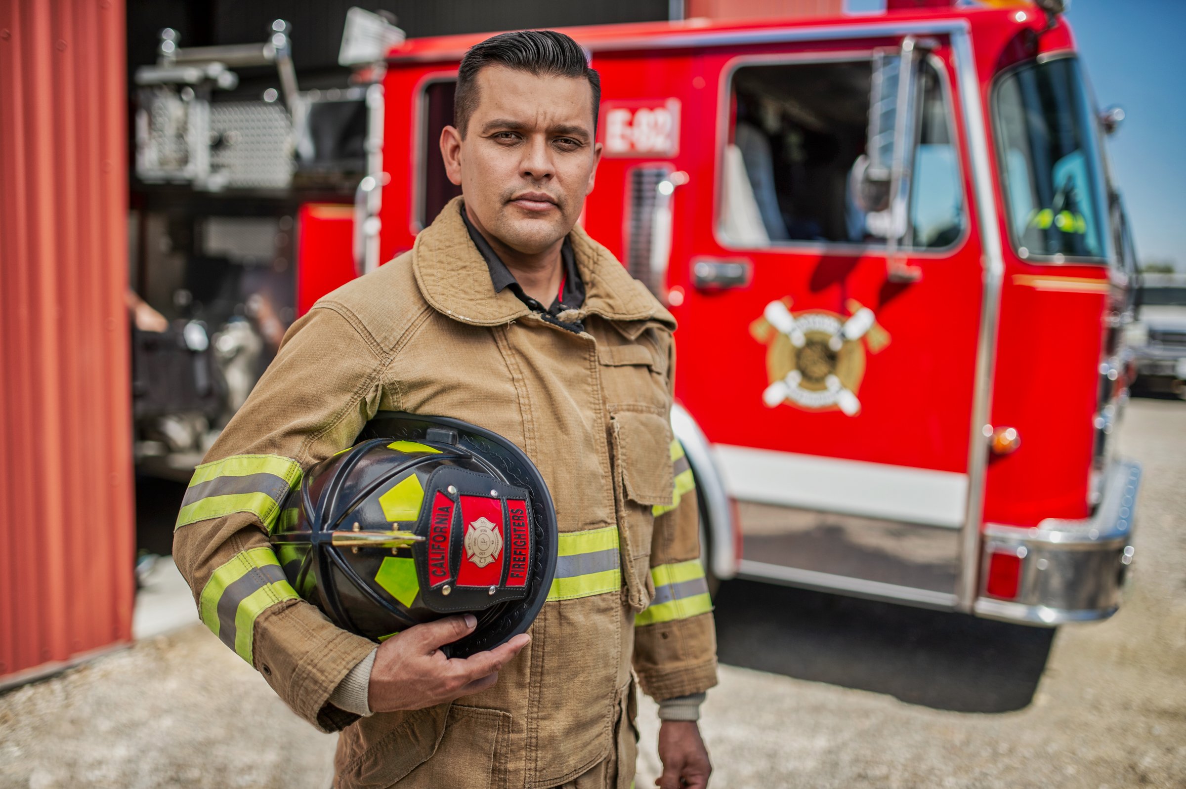 Firefighter in gear holding helmet beside fire truck, editorial first responder portrait Sacramento