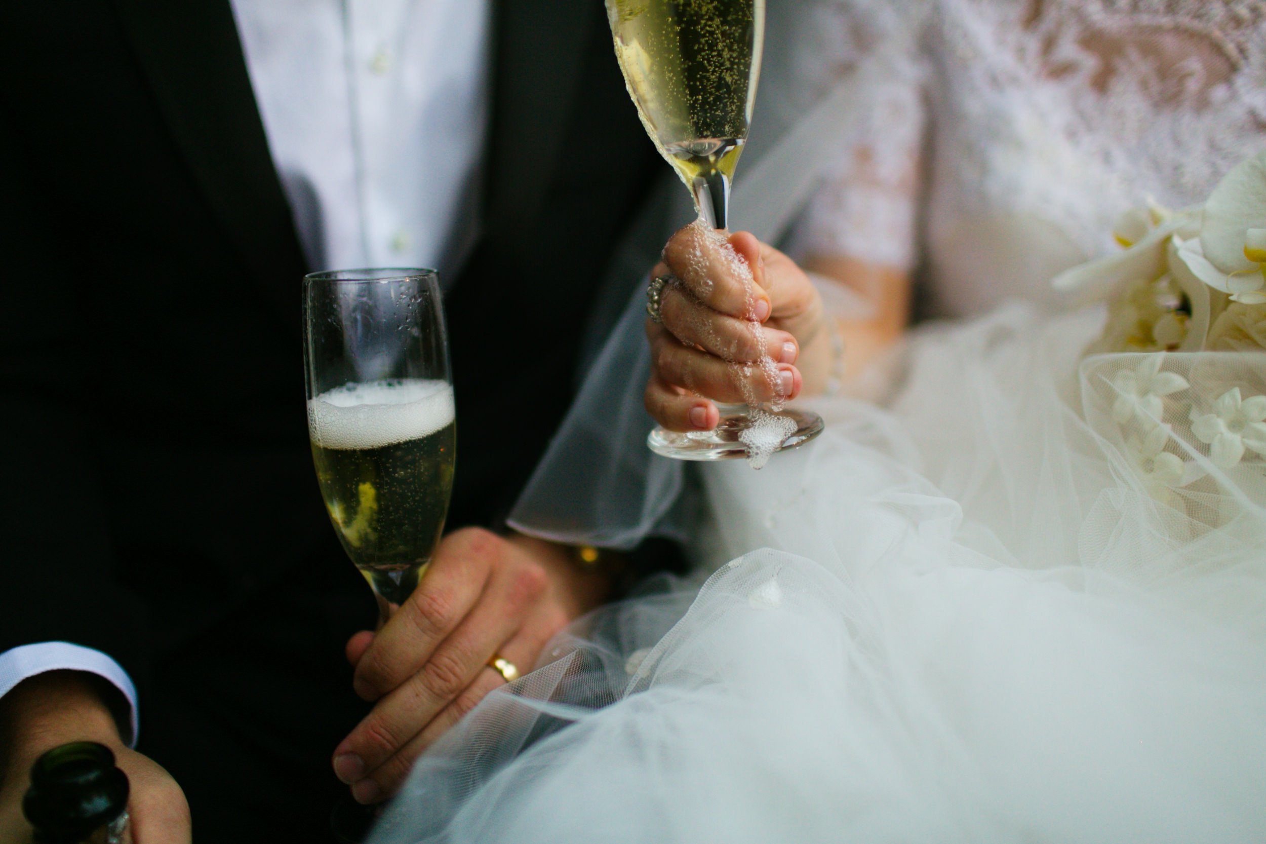 Close-up of bride and groom holding champagne glasses during their wedding celebration, with the bride pouring champagne into her glass.