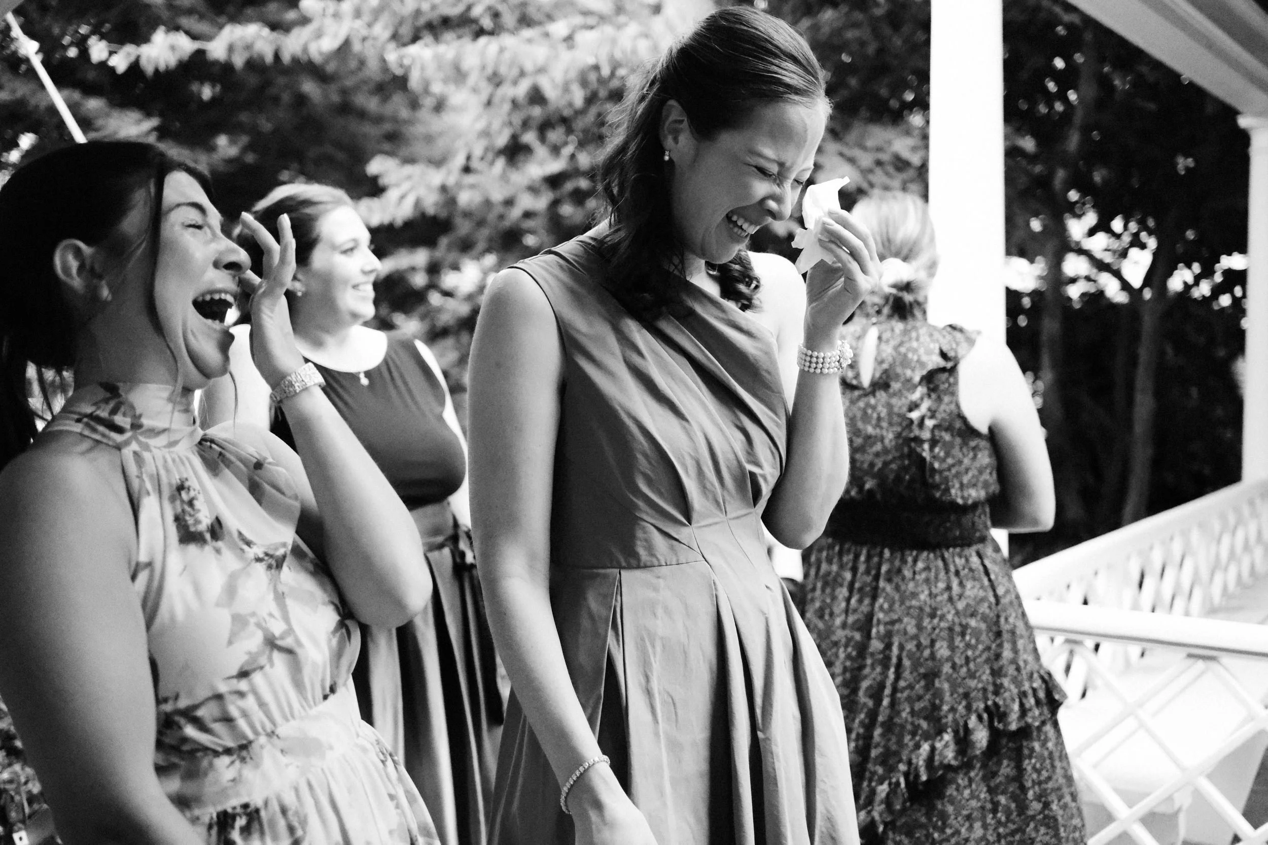 A group of women standing outside, laughing and smiling, with one woman wiping away tears of joy in the center.
