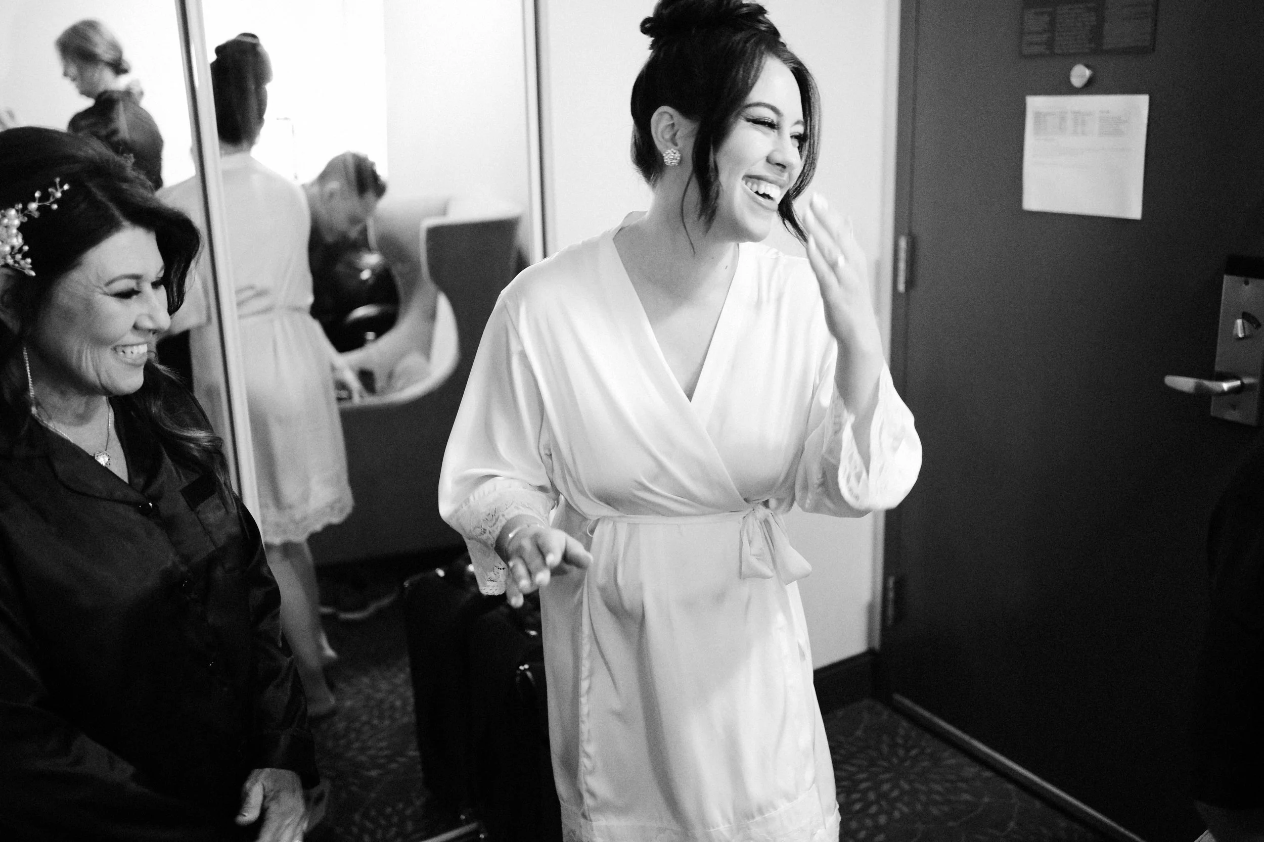 Black and white photo of women in a room, one woman in a white robe smiling and laughing, others around her also smiling and looking happy.