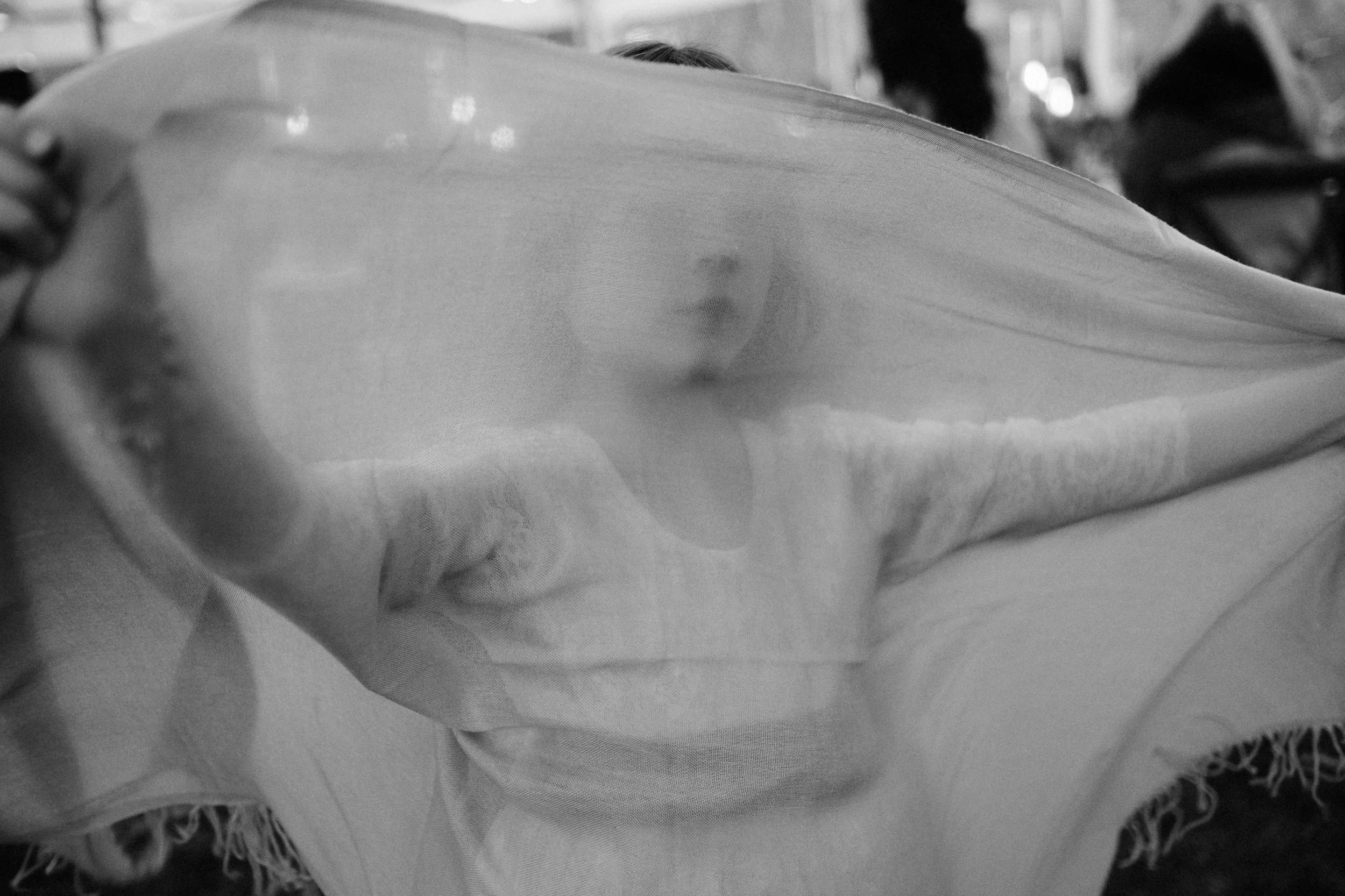 Person holding a sheer fabric in front of their face, obscuring their features, in a busy indoor setting.