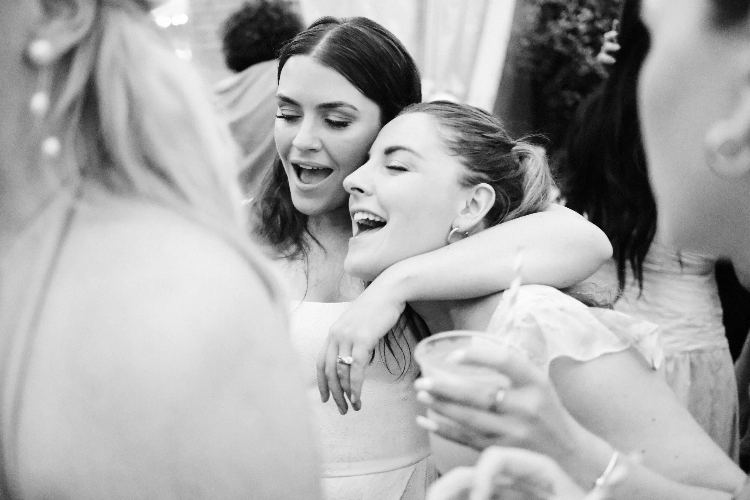 Two women joyfully hugging and singing at a celebration or party, sharing a happy moment.