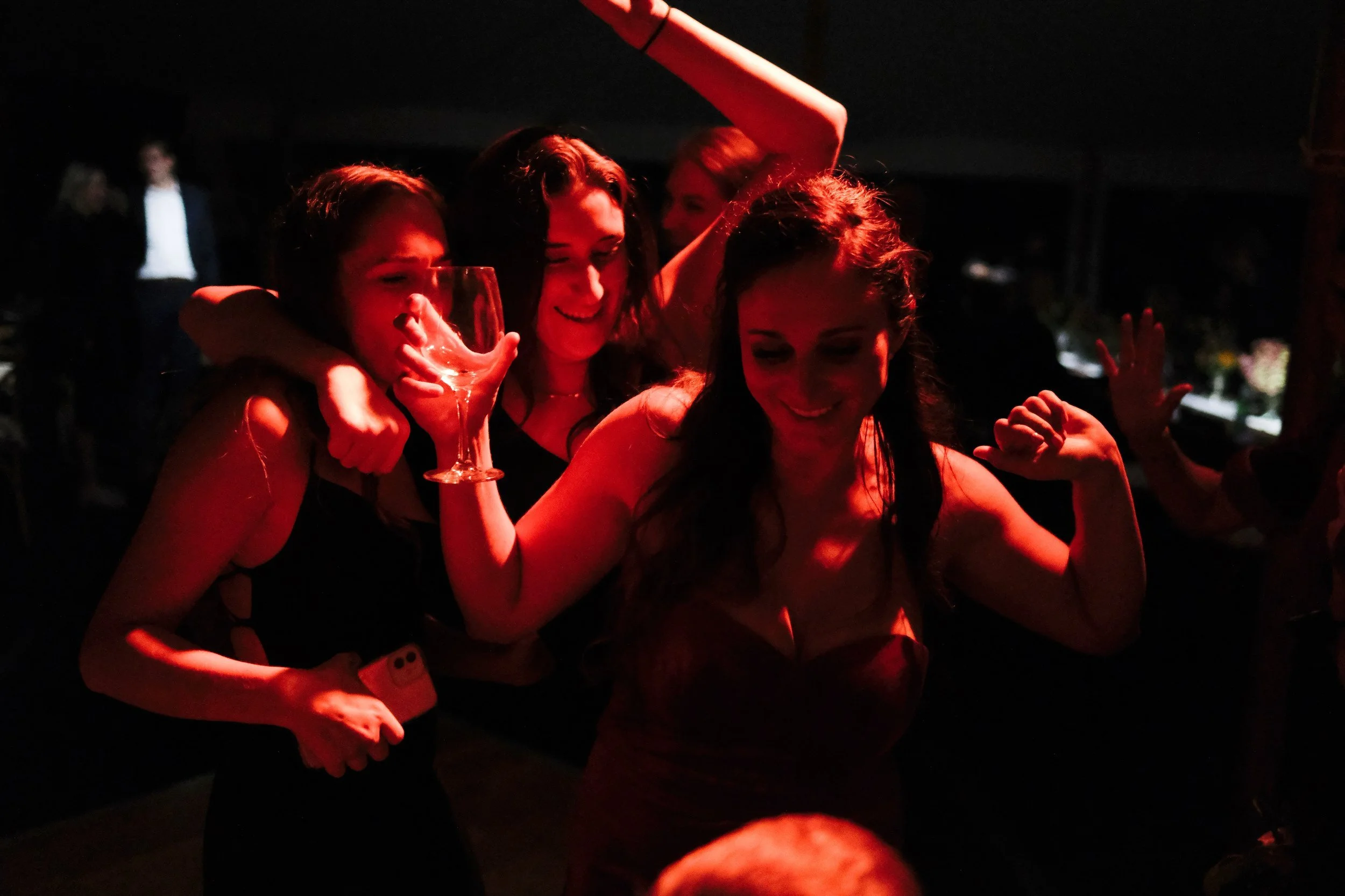 Three women dancing and celebrating with drinks at a party.