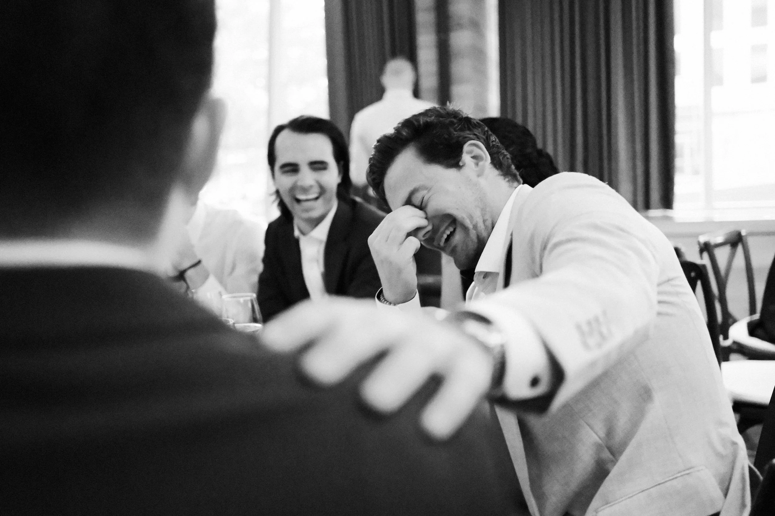 Group of men in formal attire, laughing and sharing a moment during a social gathering or meeting.