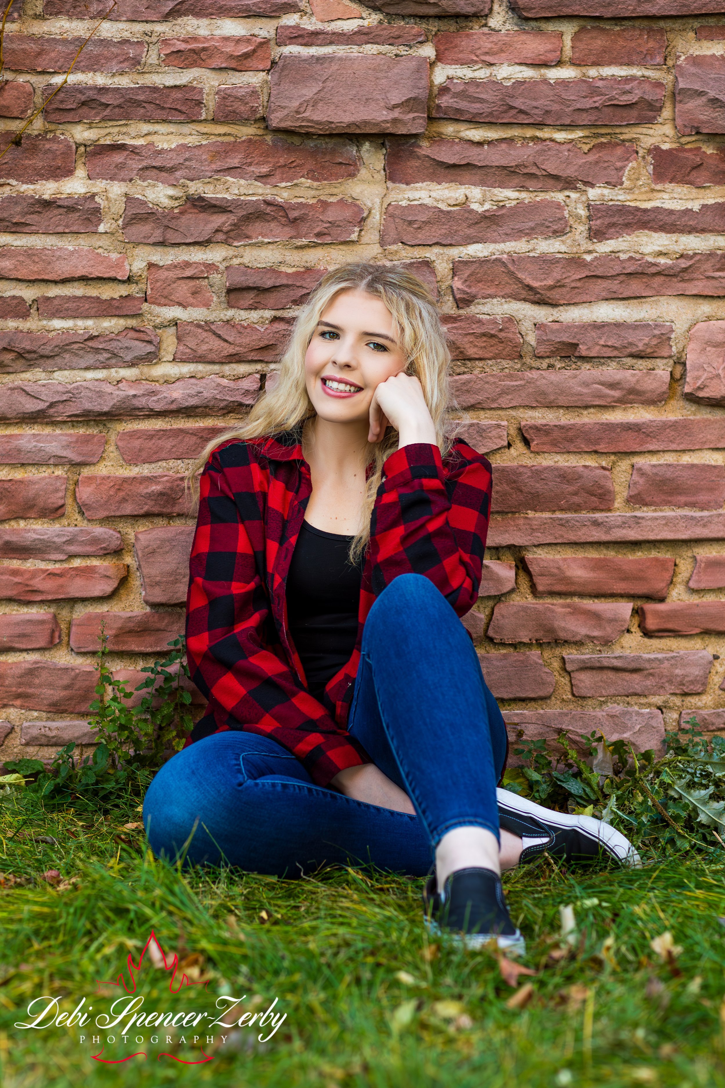 Outdoor photo of high school senior sitting against a wall.