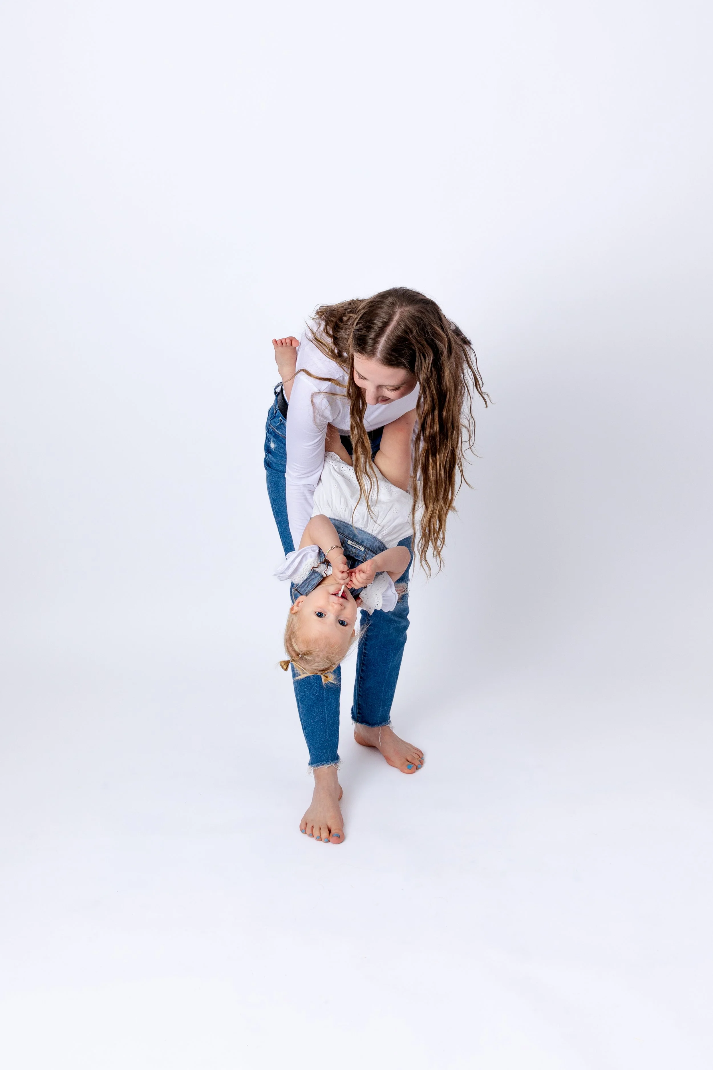 A woman playing with a young girl in a playful pose against a plain white background.