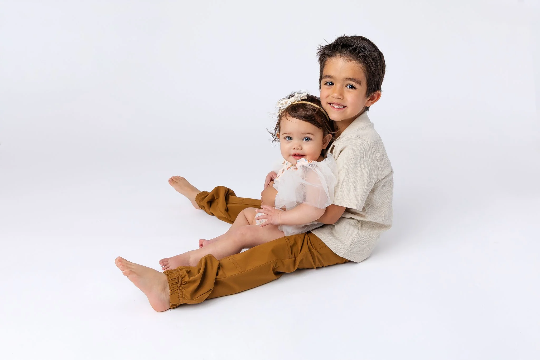 A young boy and a little girl sitting on the floor against a plain white background in Cheyenne, Wy. 