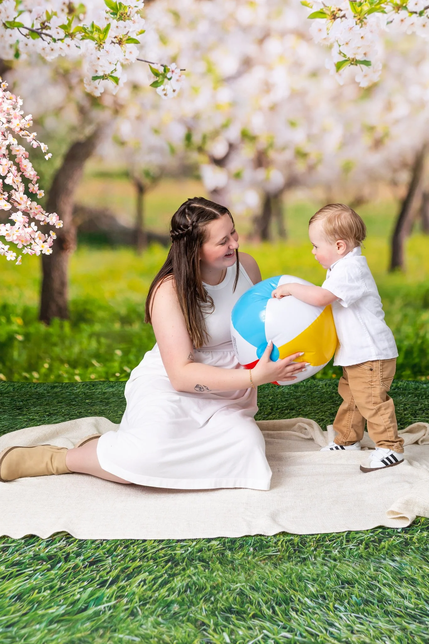 A woman and a young boy playing with a beach ball outdoors among blooming trees.