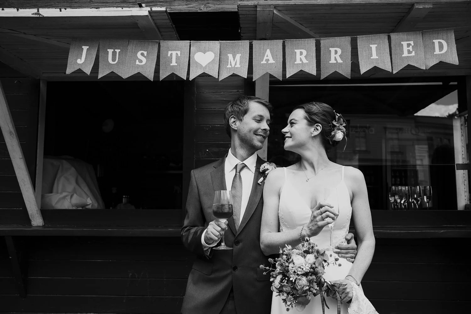 Braut und Bräutigam trinken Wein unter einem "Just Married"-Schild.