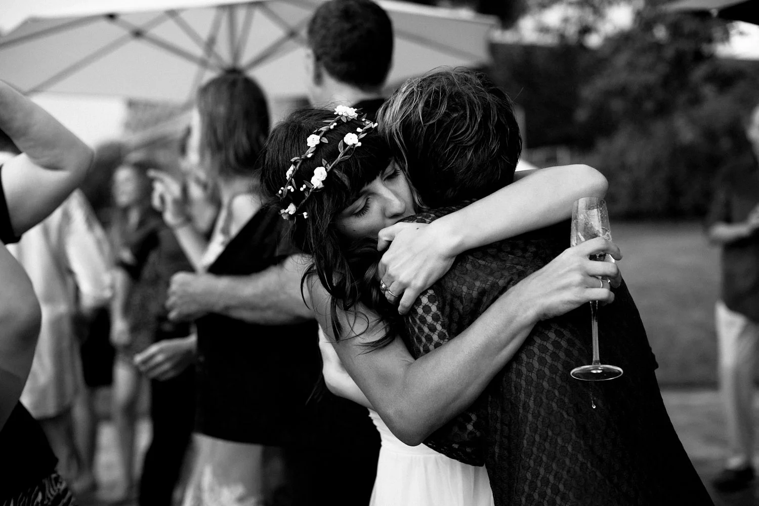 Bride hugging wedding guest while holding a glass of sparkling wine.