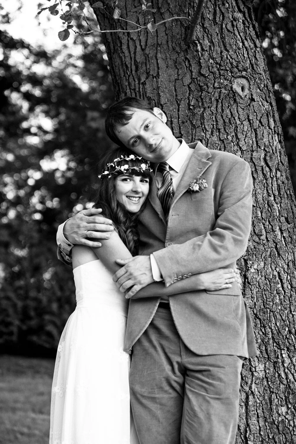 Bride and groom leaning against a tree.