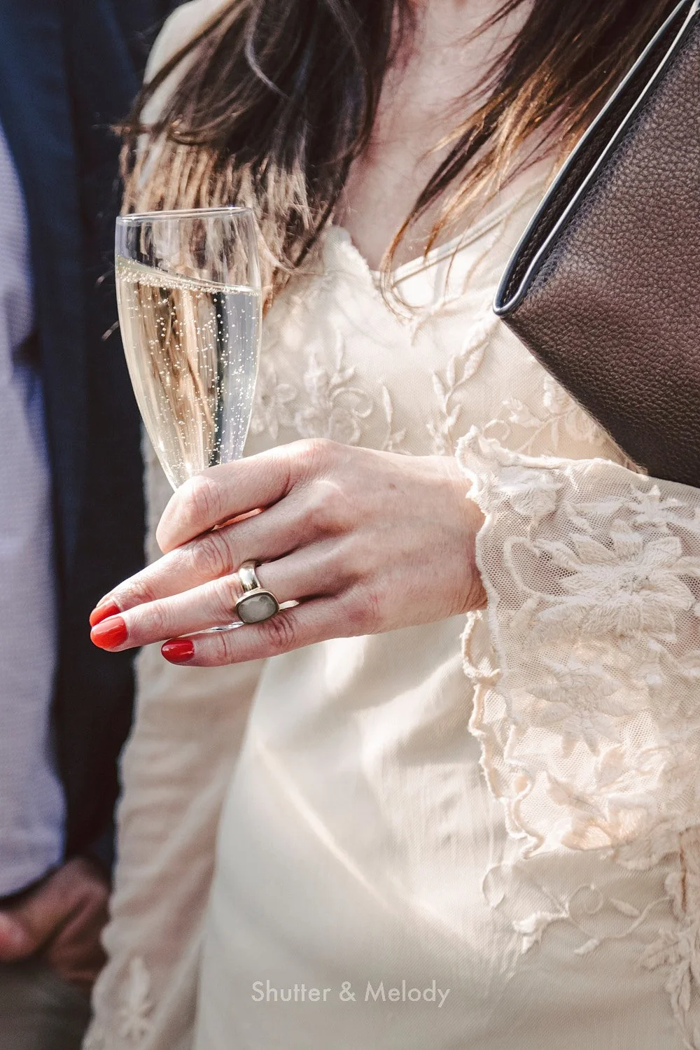 A close-up of a wedding guest's hand holding a glass of sparkling wine.
