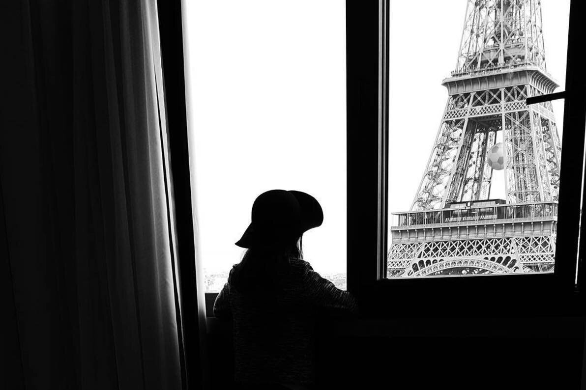 Girl admiring the Eiffel Tower from her hotel room's window